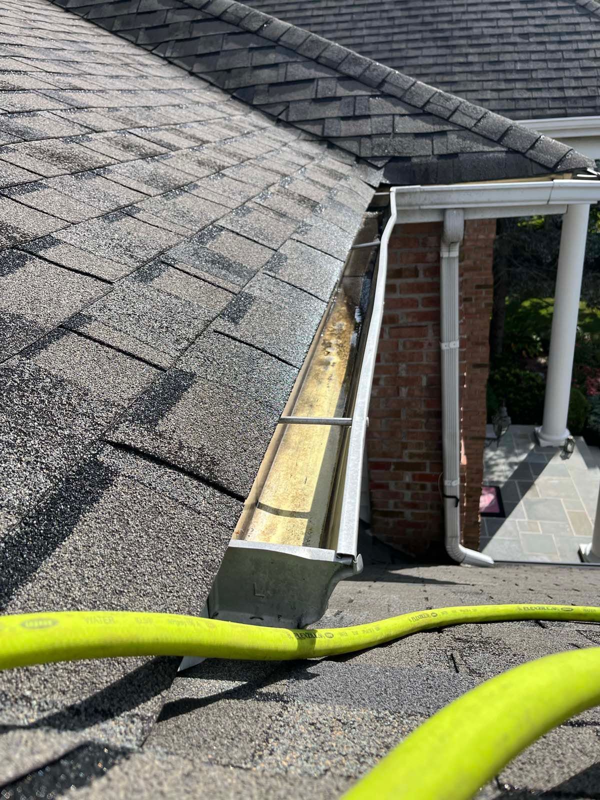 A yellow hose is attached to a gutter on the roof of a house.