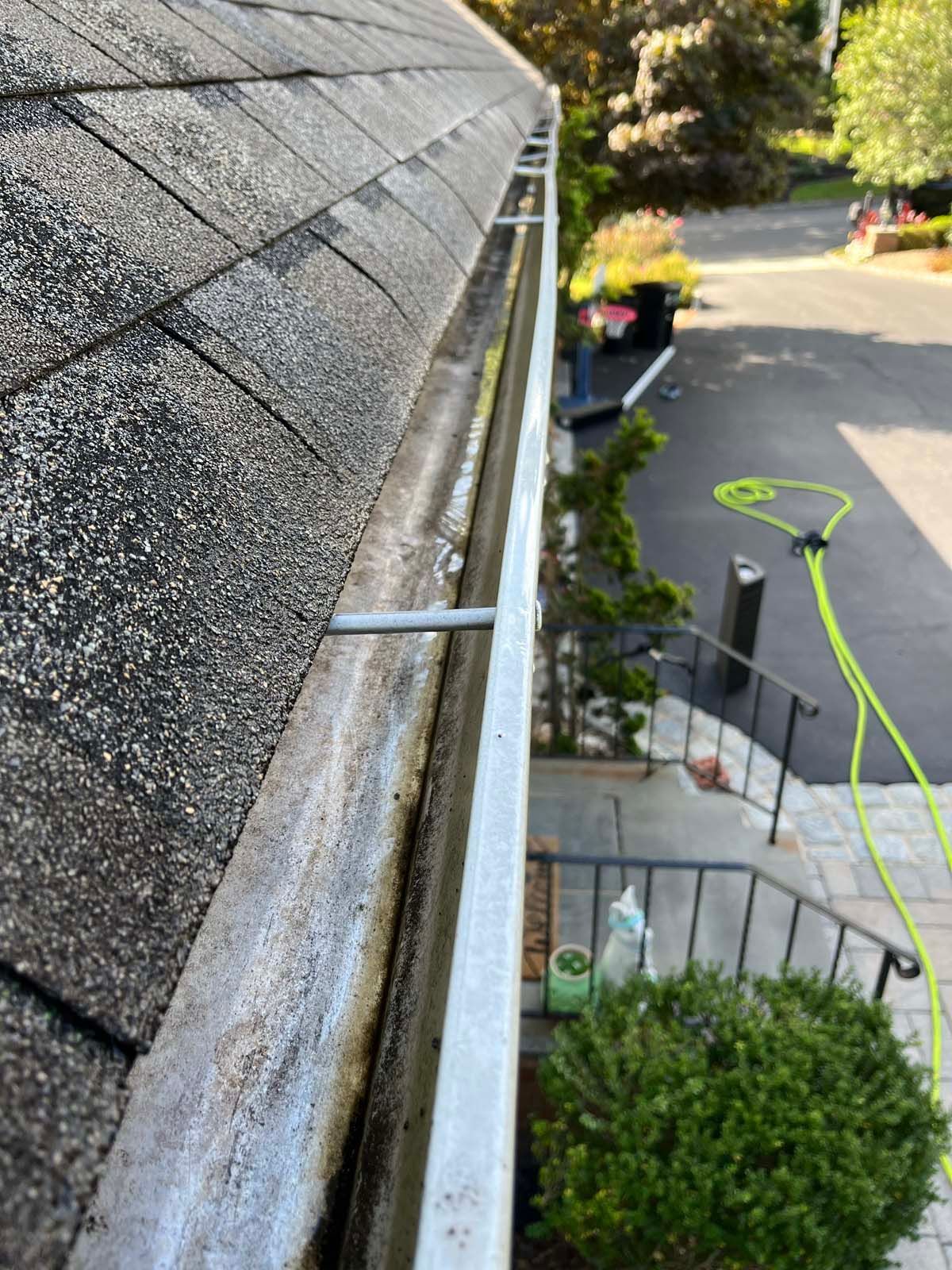 A close up of a gutter on a roof with a green hose attached to it.