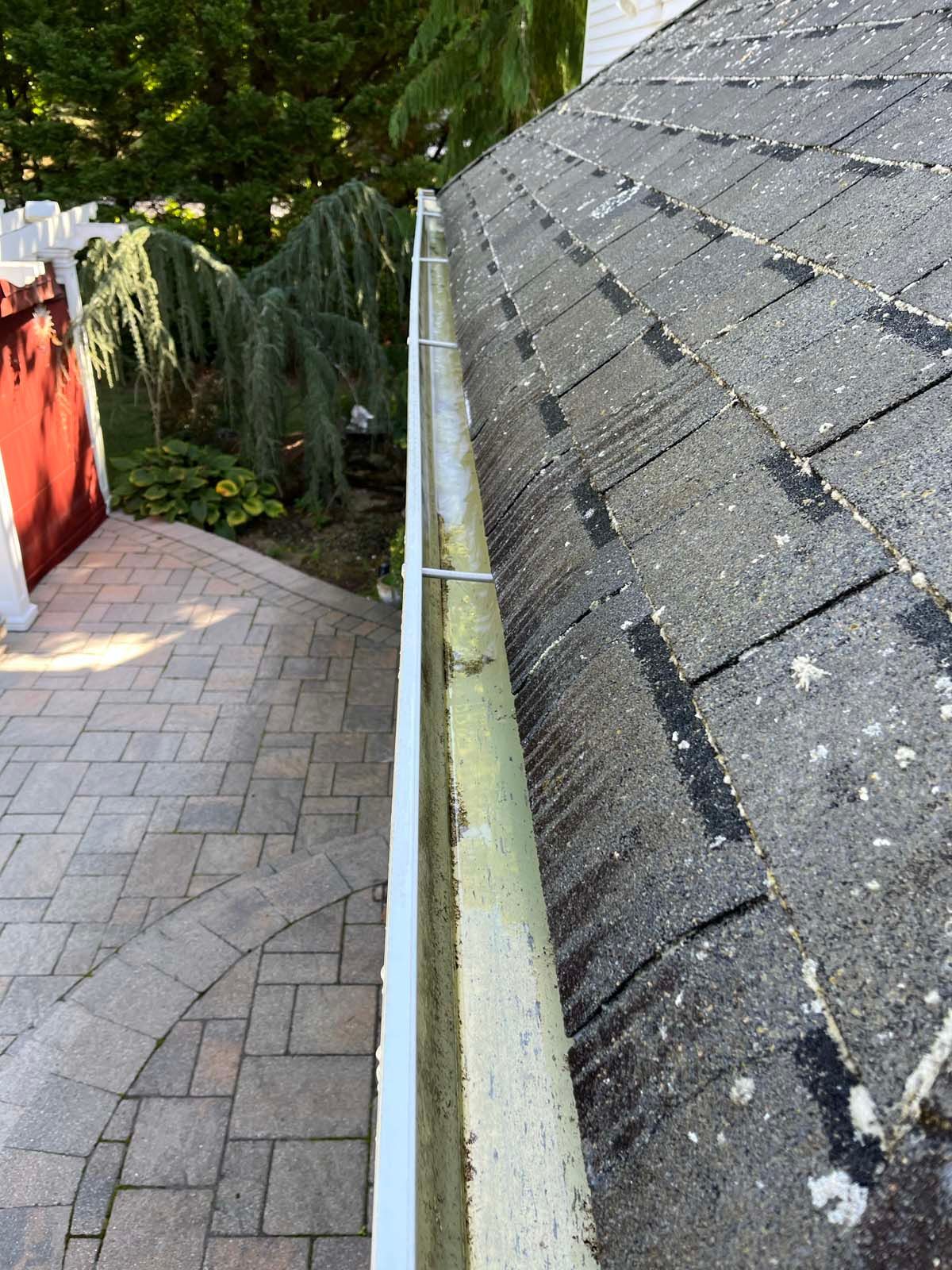 A gutter on the side of a roof next to a brick walkway.