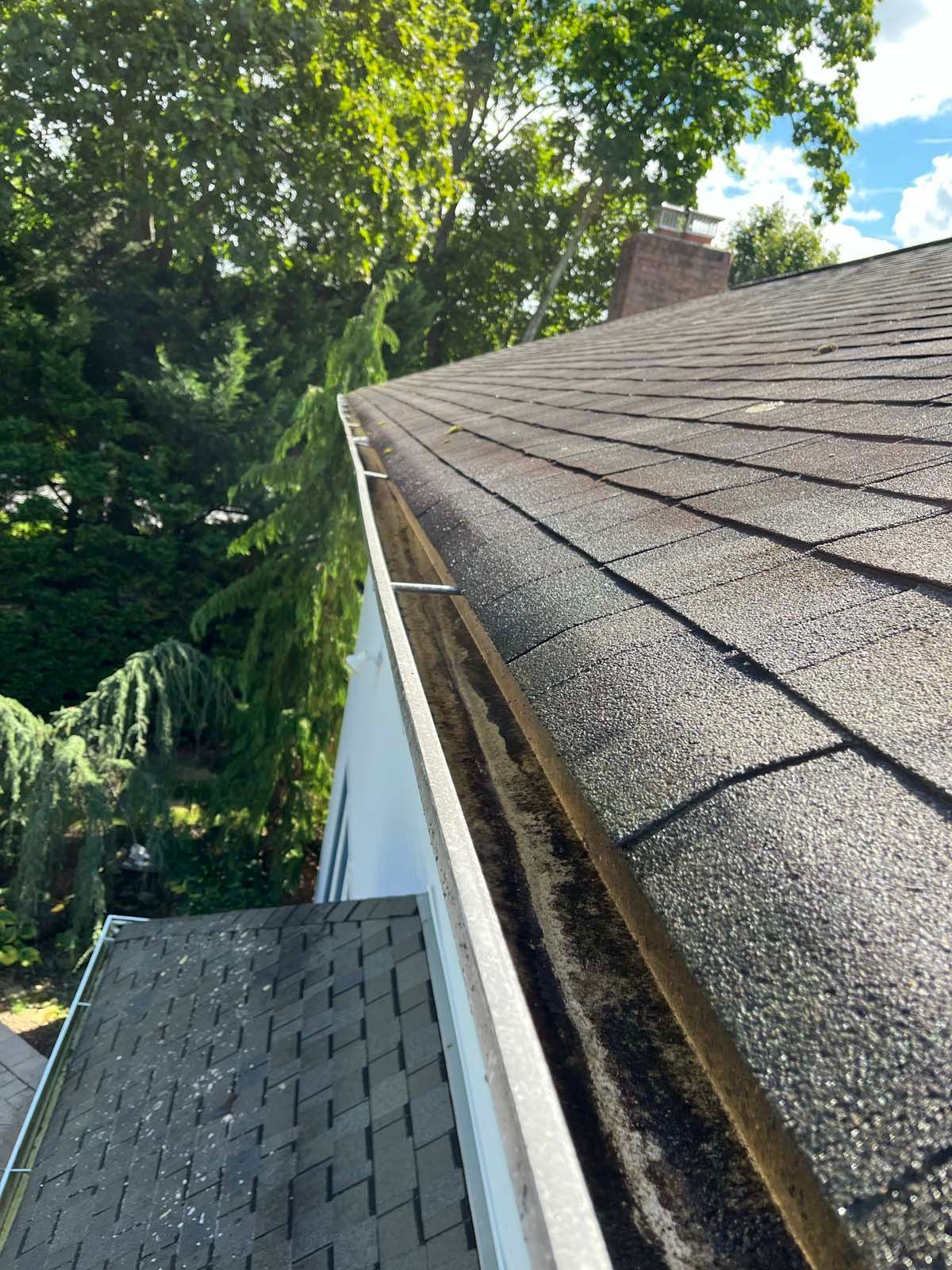A gutter on the roof of a house with trees in the background.