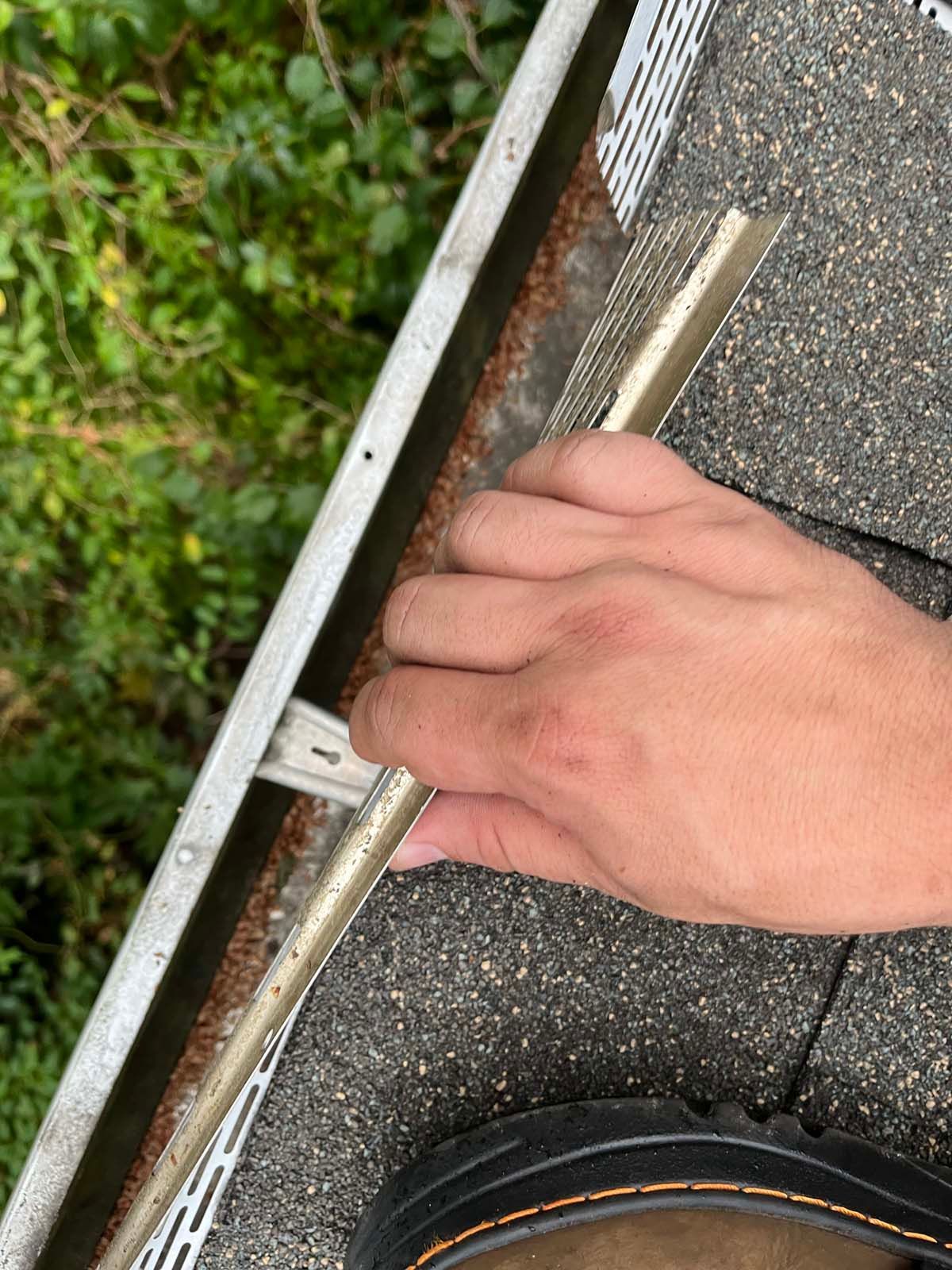 A person is cleaning a gutter on a roof with a brush.