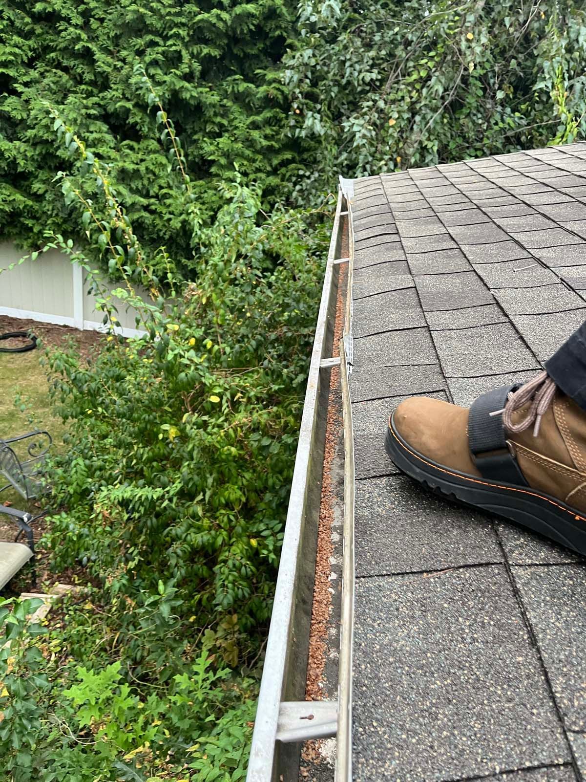 A person is standing on a roof next to a gutter.