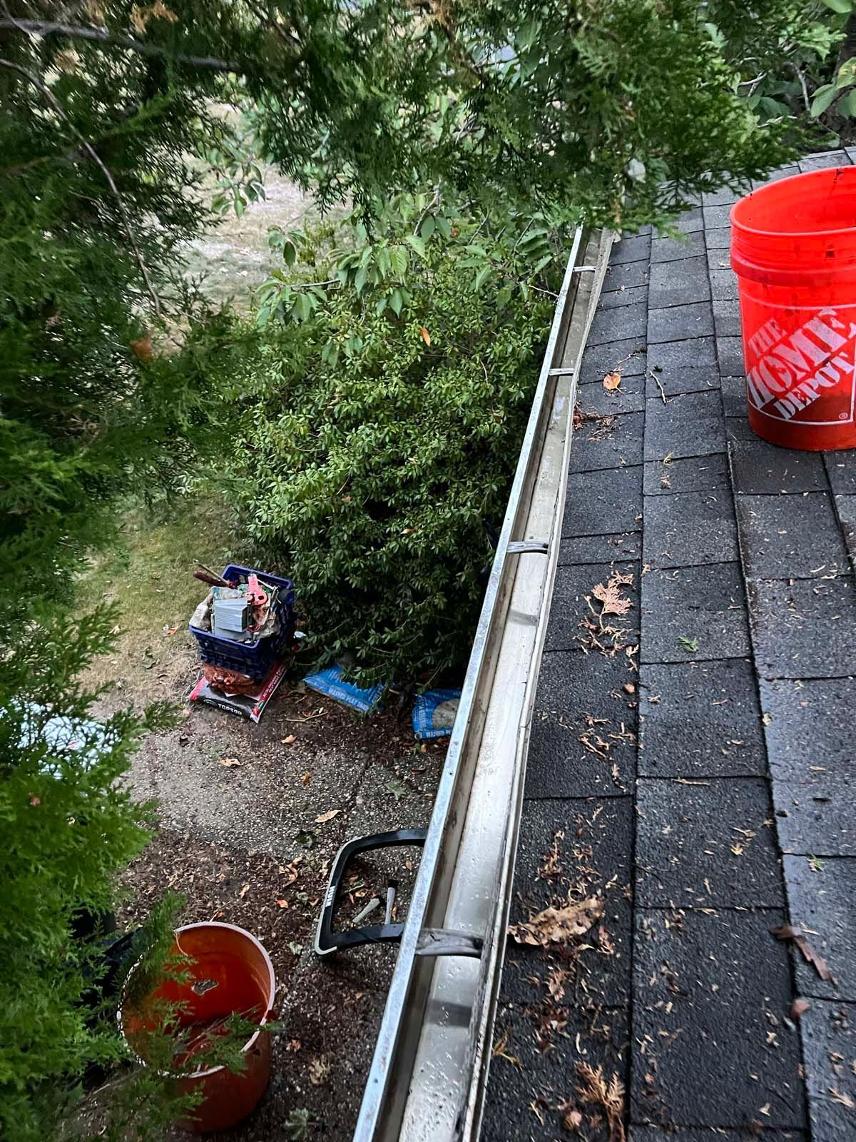 A red bucket is sitting on top of a roof next to a gutter.