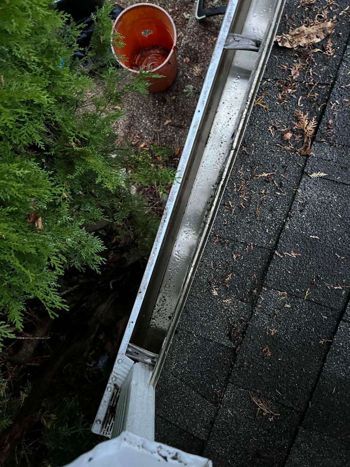 A person is cleaning a gutter on a roof with a bucket.