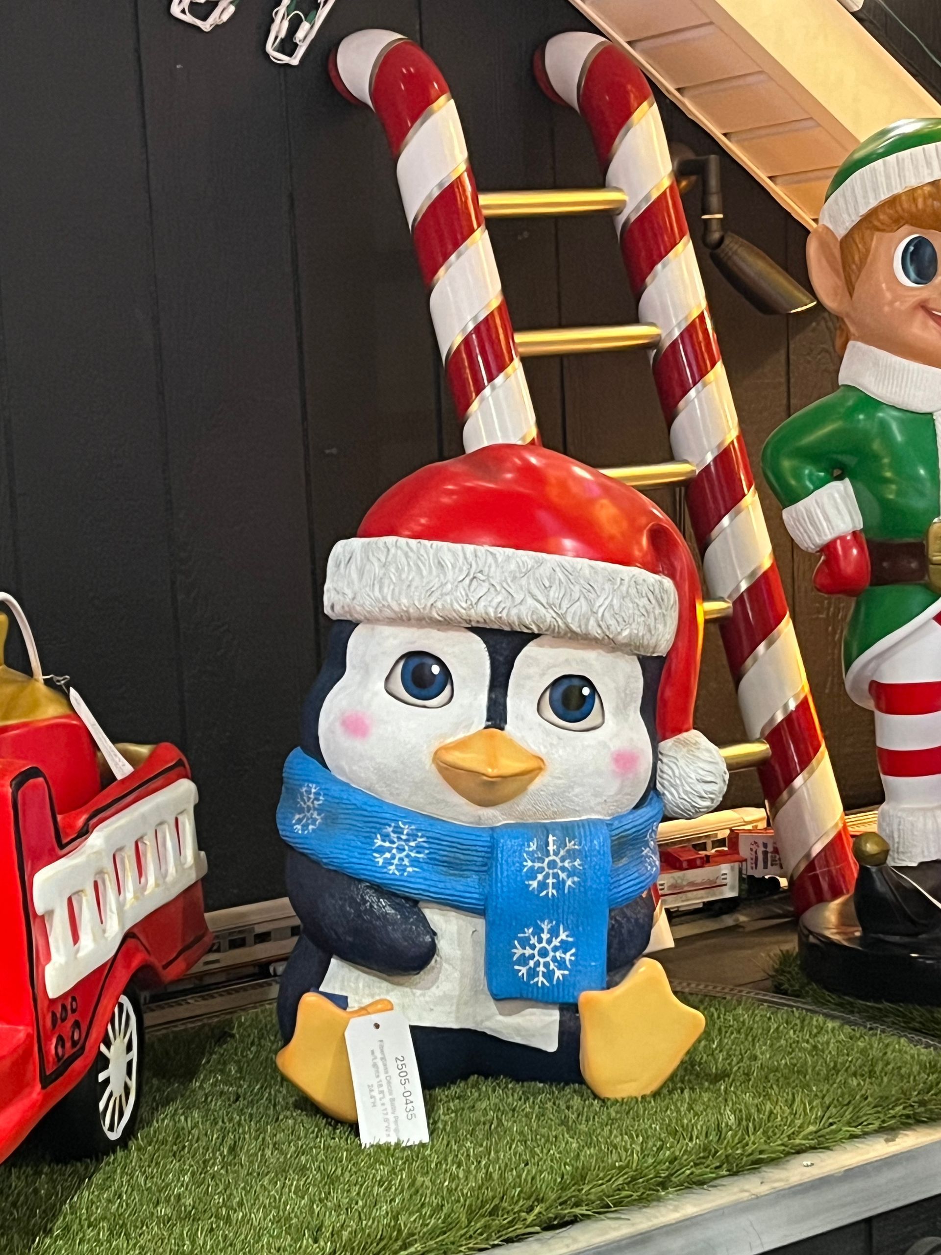 A penguin wearing a santa hat and scarf is sitting next to a candy cane ladder.
