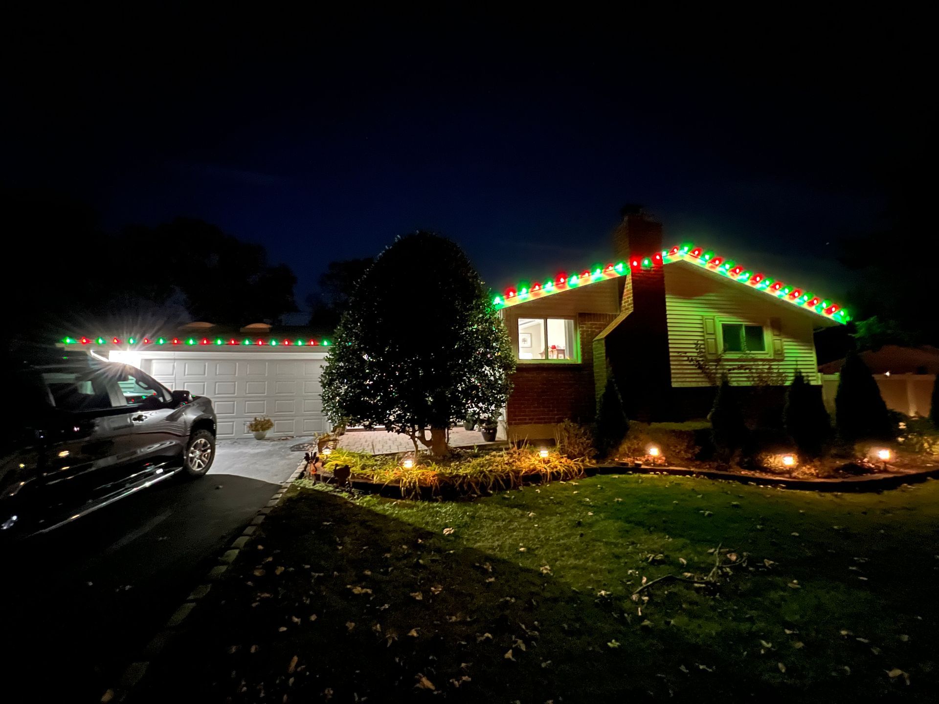 A house with christmas lights on the roof is lit up at night.