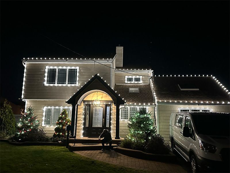House at night with Christmas lights. White lights frame windows, rooflines. Van parked.