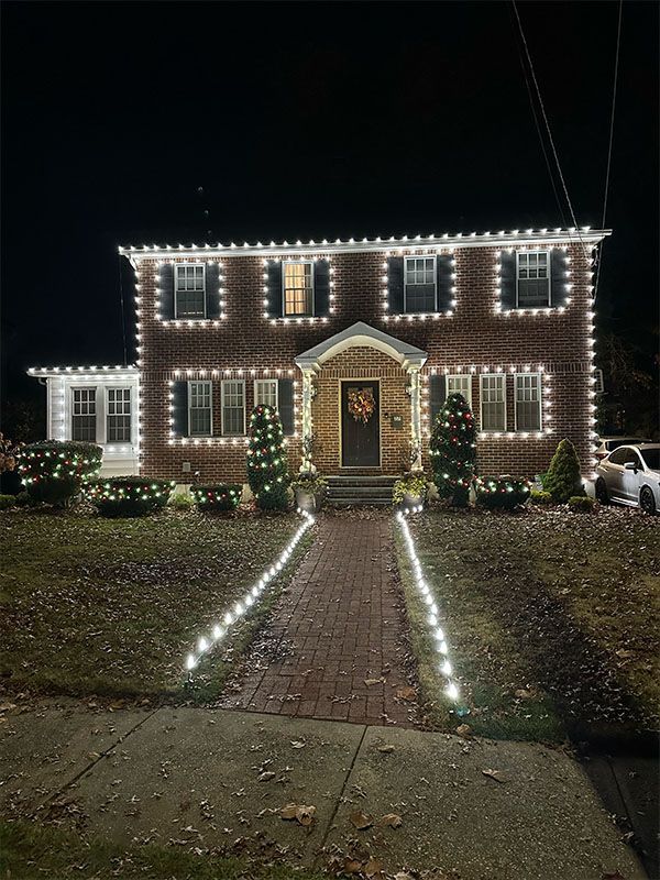 A brick house with Christmas lights outlining the roof, windows, and walkway at night.