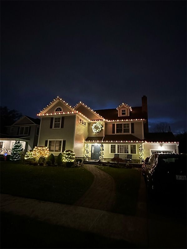 House decorated with Christmas lights at night, with a wreath on the front door.