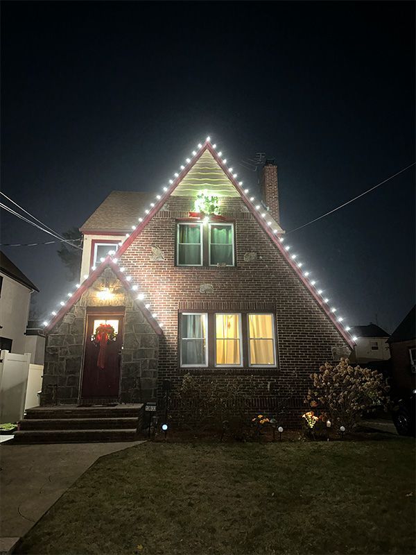 House at night decorated with white Christmas lights outlining the roof, and a wreath on the door.