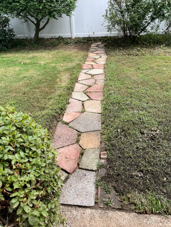 A stone walkway leading to a white fence in a backyard.