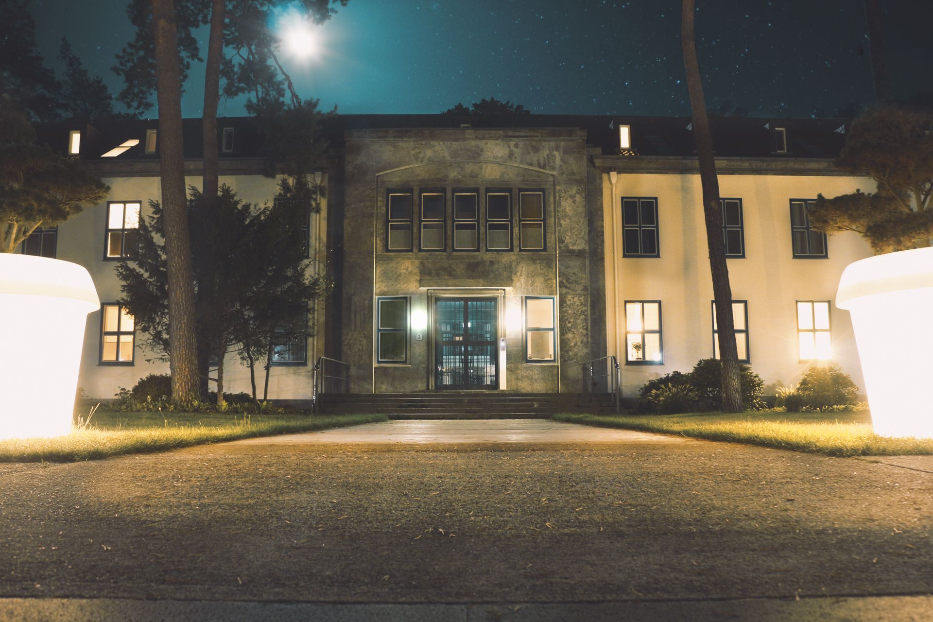 Night view of a lit two-story building with a central entrance and moon above the roof