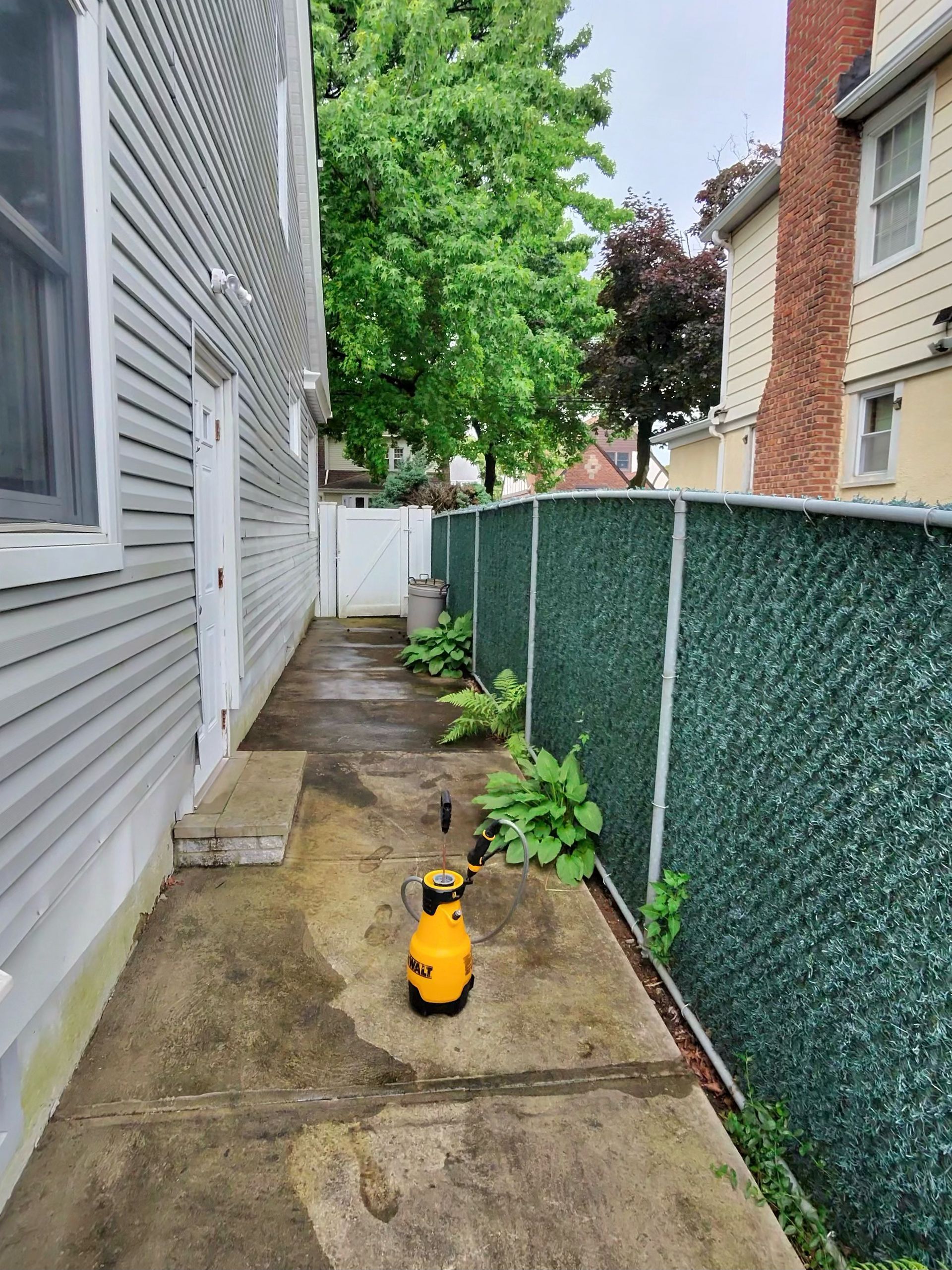 A yellow spray bottle is sitting on the sidewalk next to a fence.
