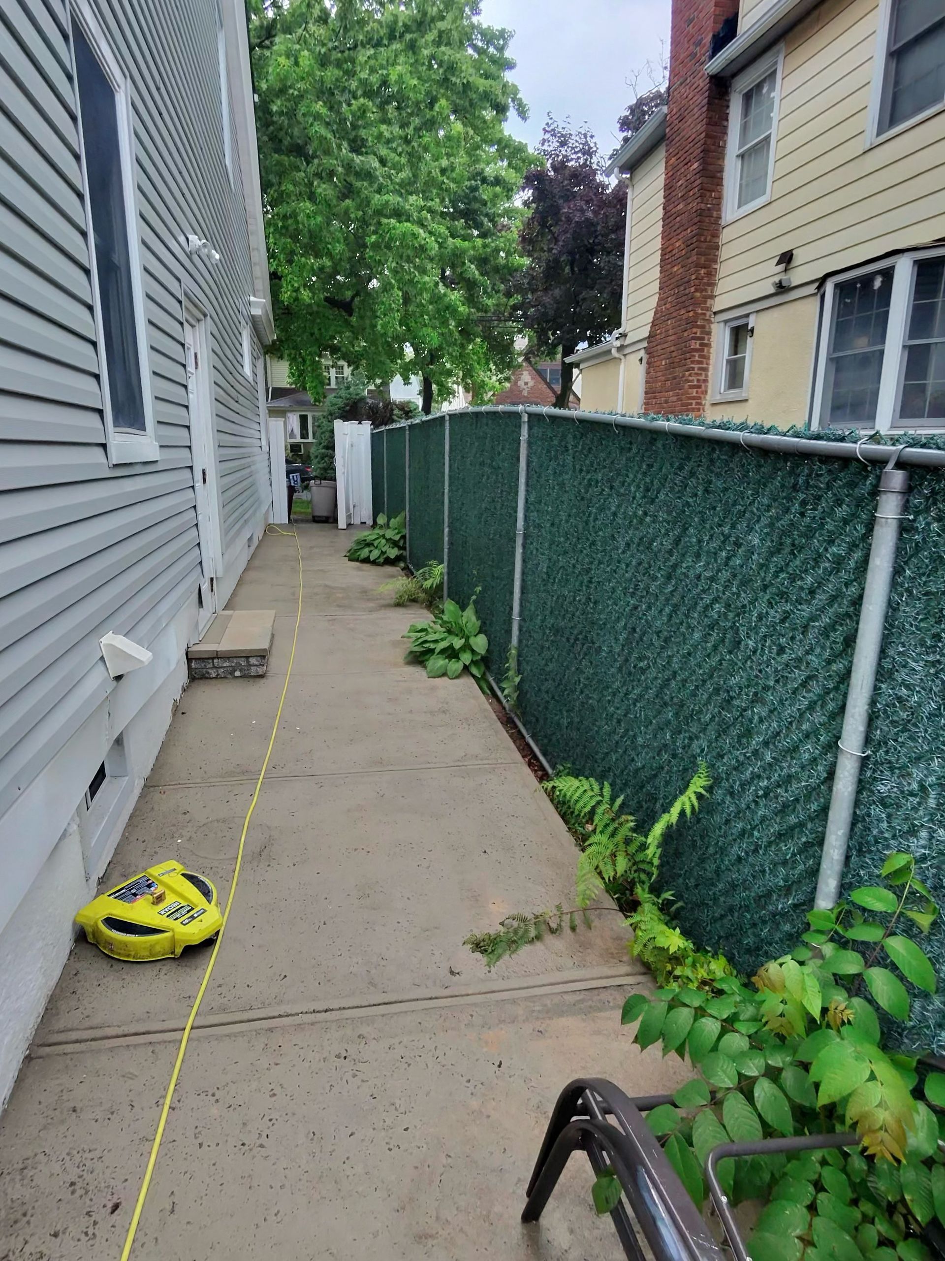 A yellow tape measure is sitting on the sidewalk next to a fence.