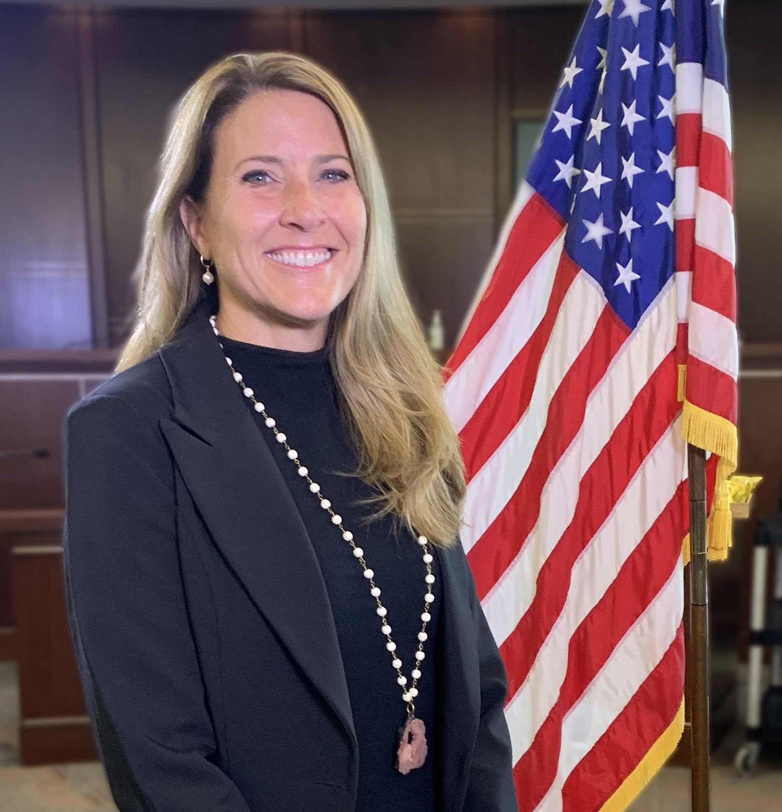 A woman is smiling in front of an american flag