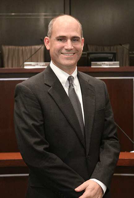 A man in a blue suit is leaning against a stone wall.