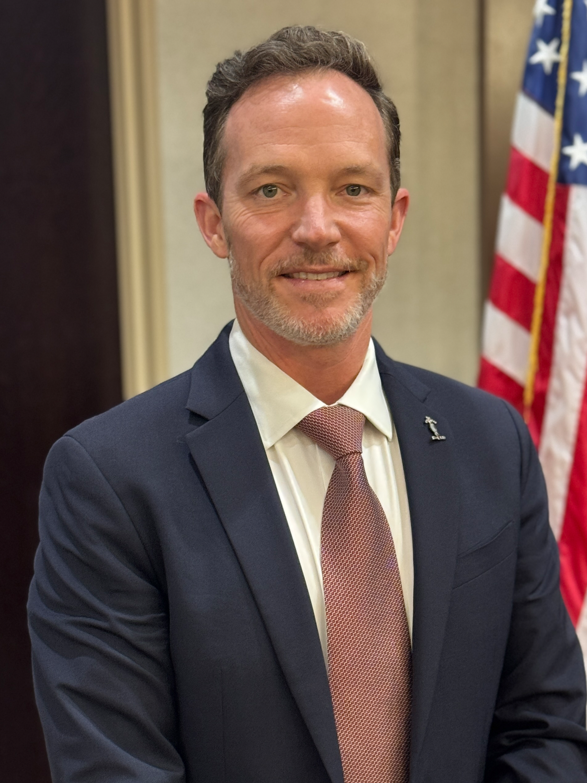 A man in a suit is standing in front of an american flag.