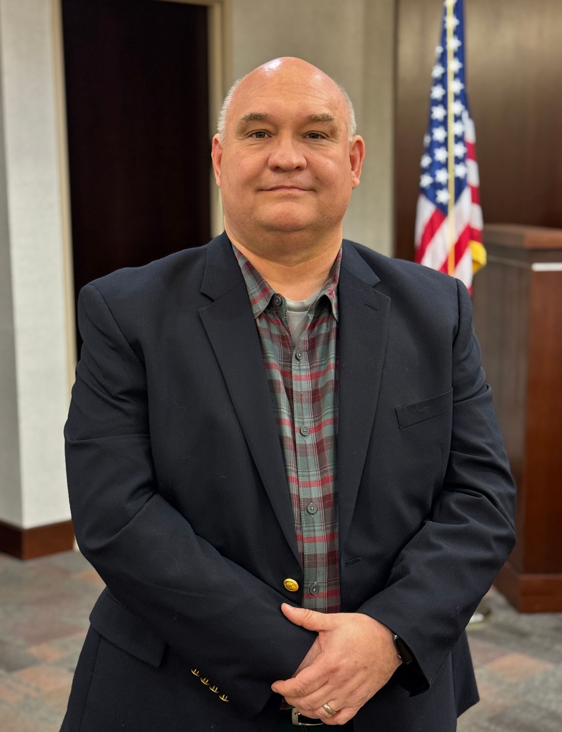 A man in a suit and tie is standing in front of an american flag.
