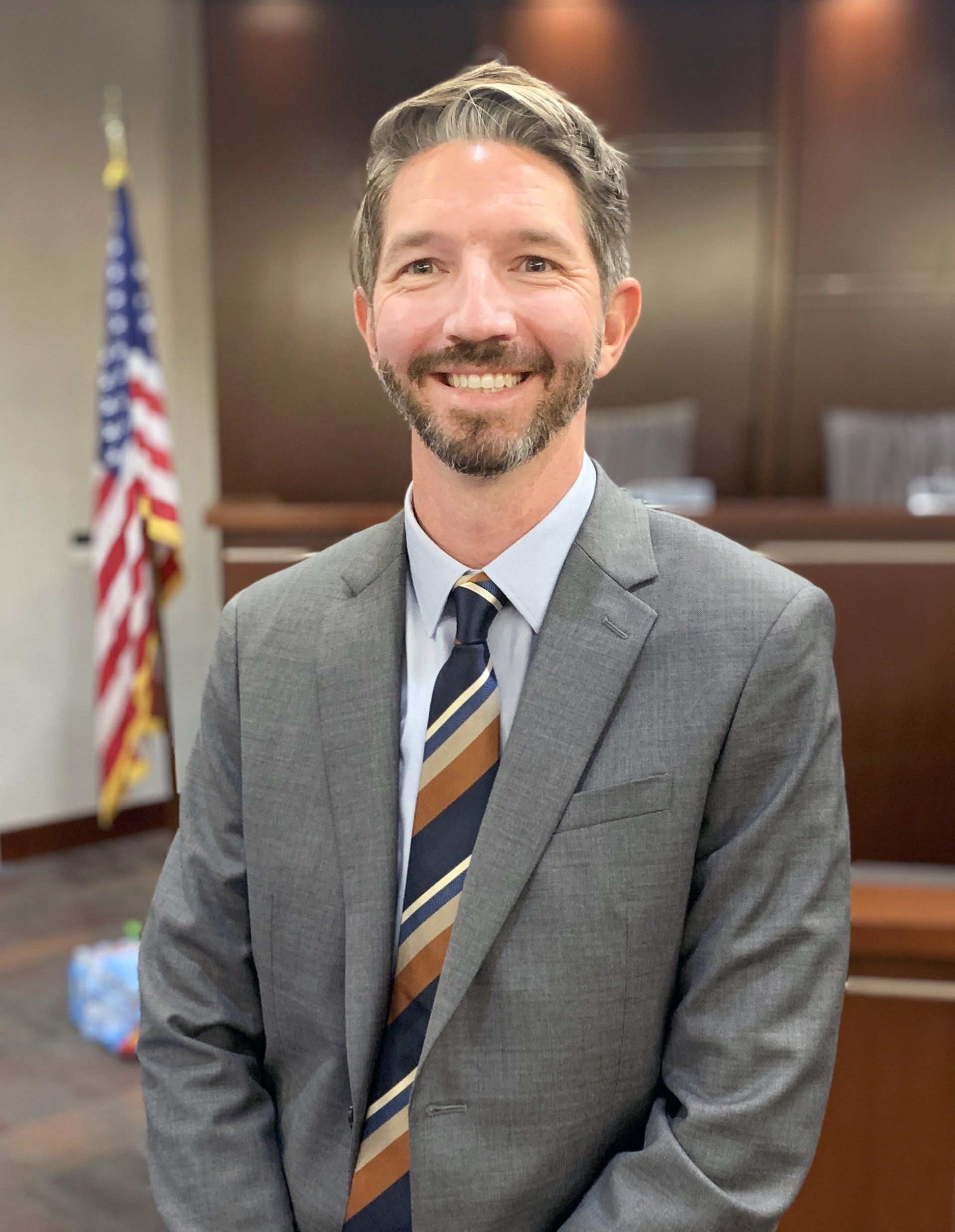 A man in a suit and tie is standing in front of an american flag.