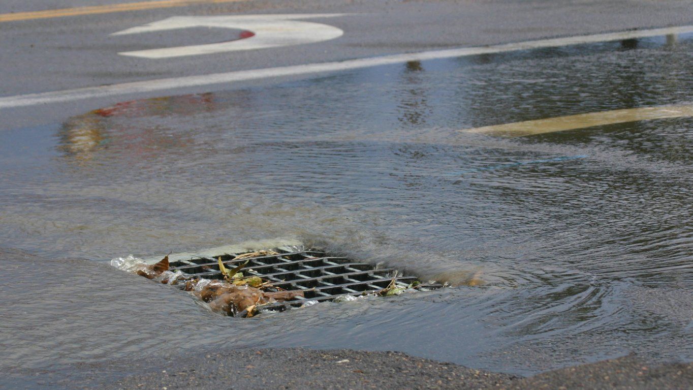 A manhole cover is filled with water on a wet street.