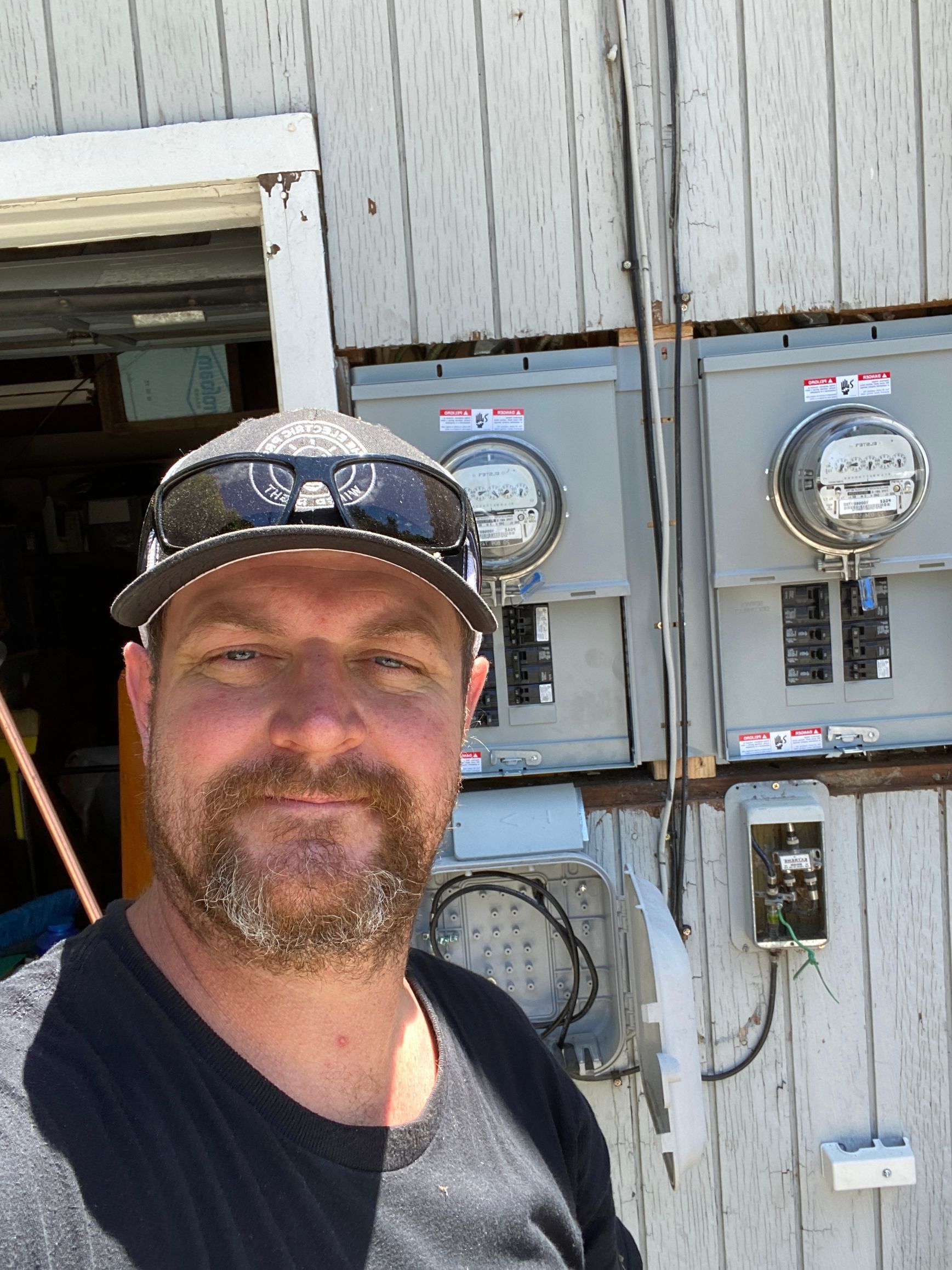 The Electric Pro - A man with a beard is standing in front of a building with electrical panels.