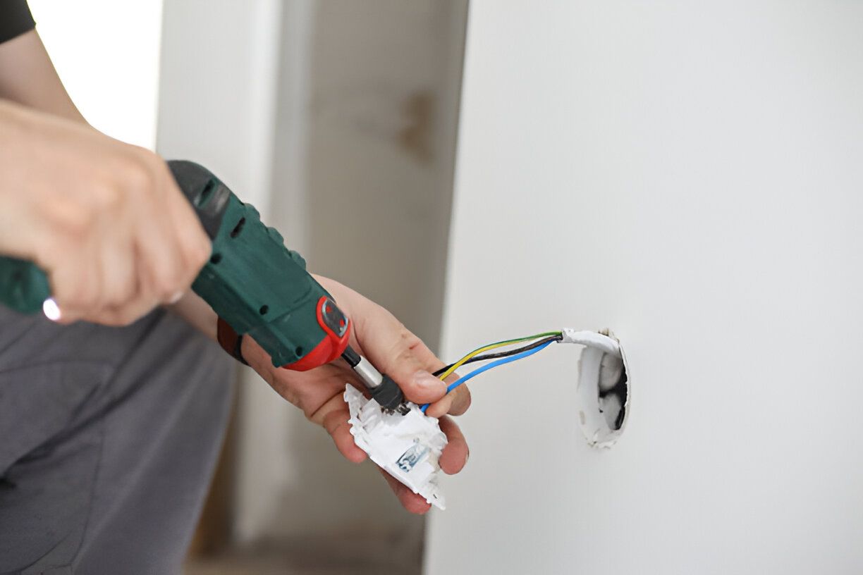 The Electric Pro - A person is installing a light switch on a wall with a drill.