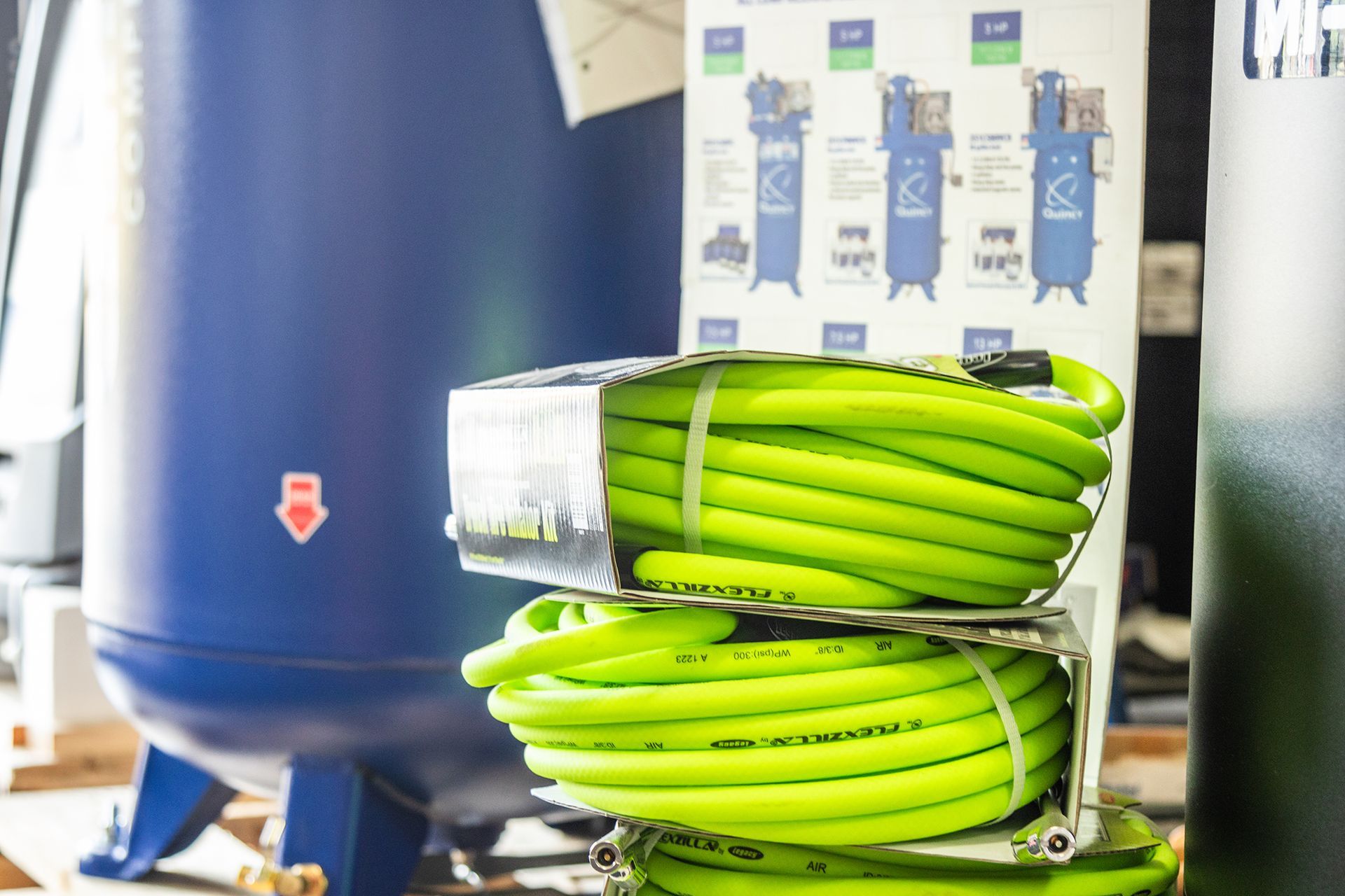 A green hose is stacked on top of each other in front of a blue tank.
