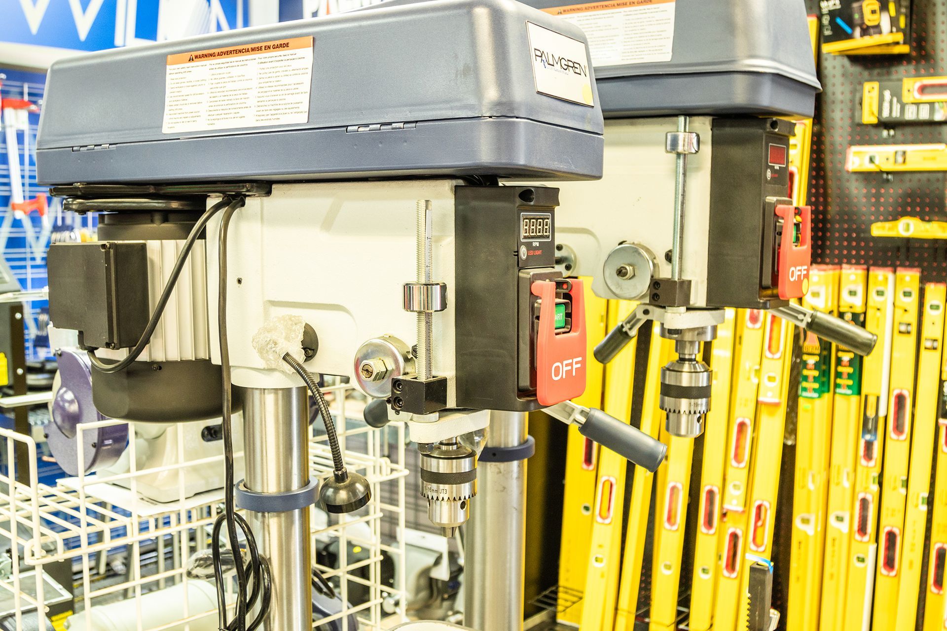 A drill press is sitting in a store next to a row of yellow level sticks.