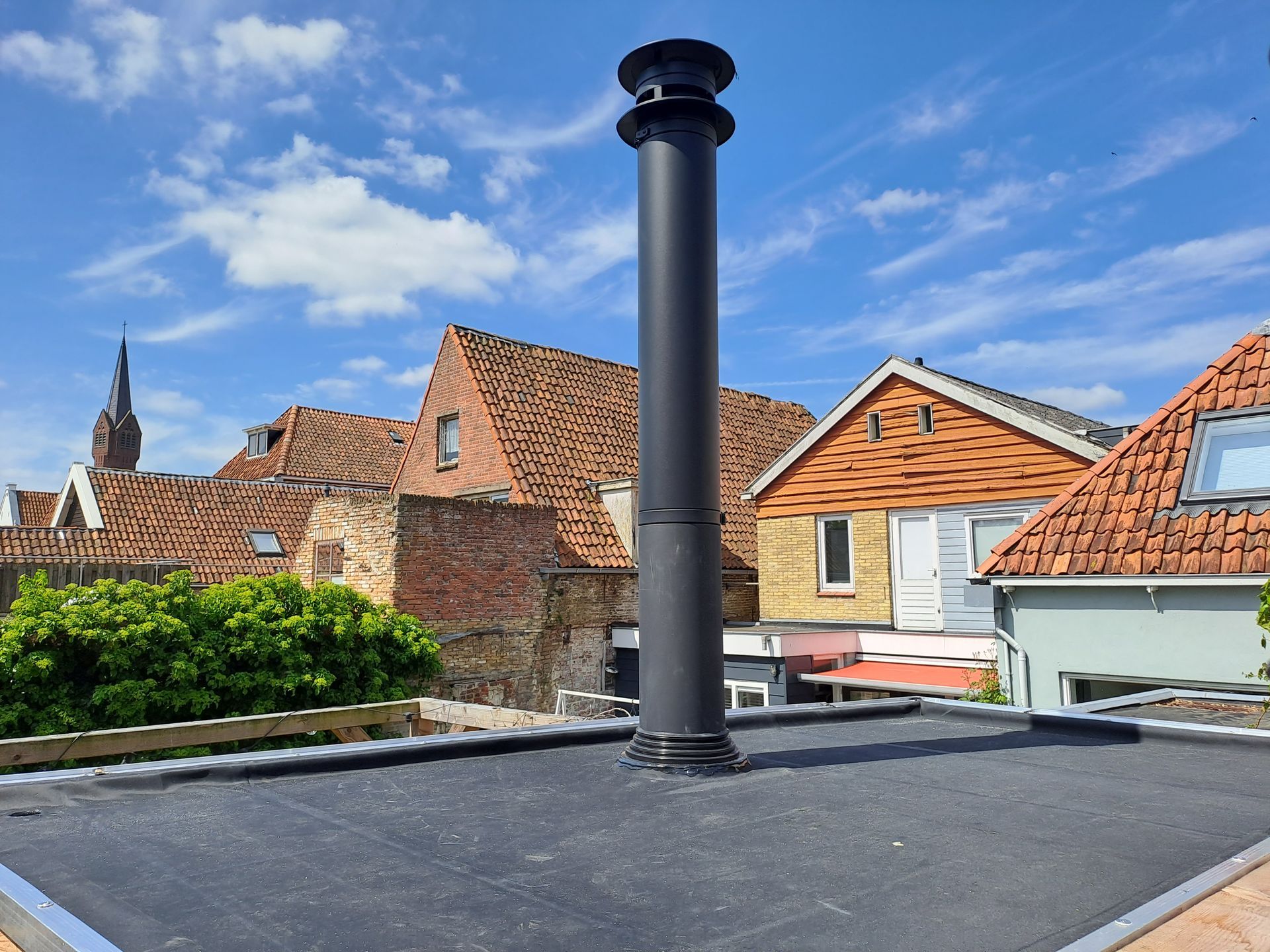 Een zwarte schoorsteen staat op een dak voor een bakstenen gebouw.