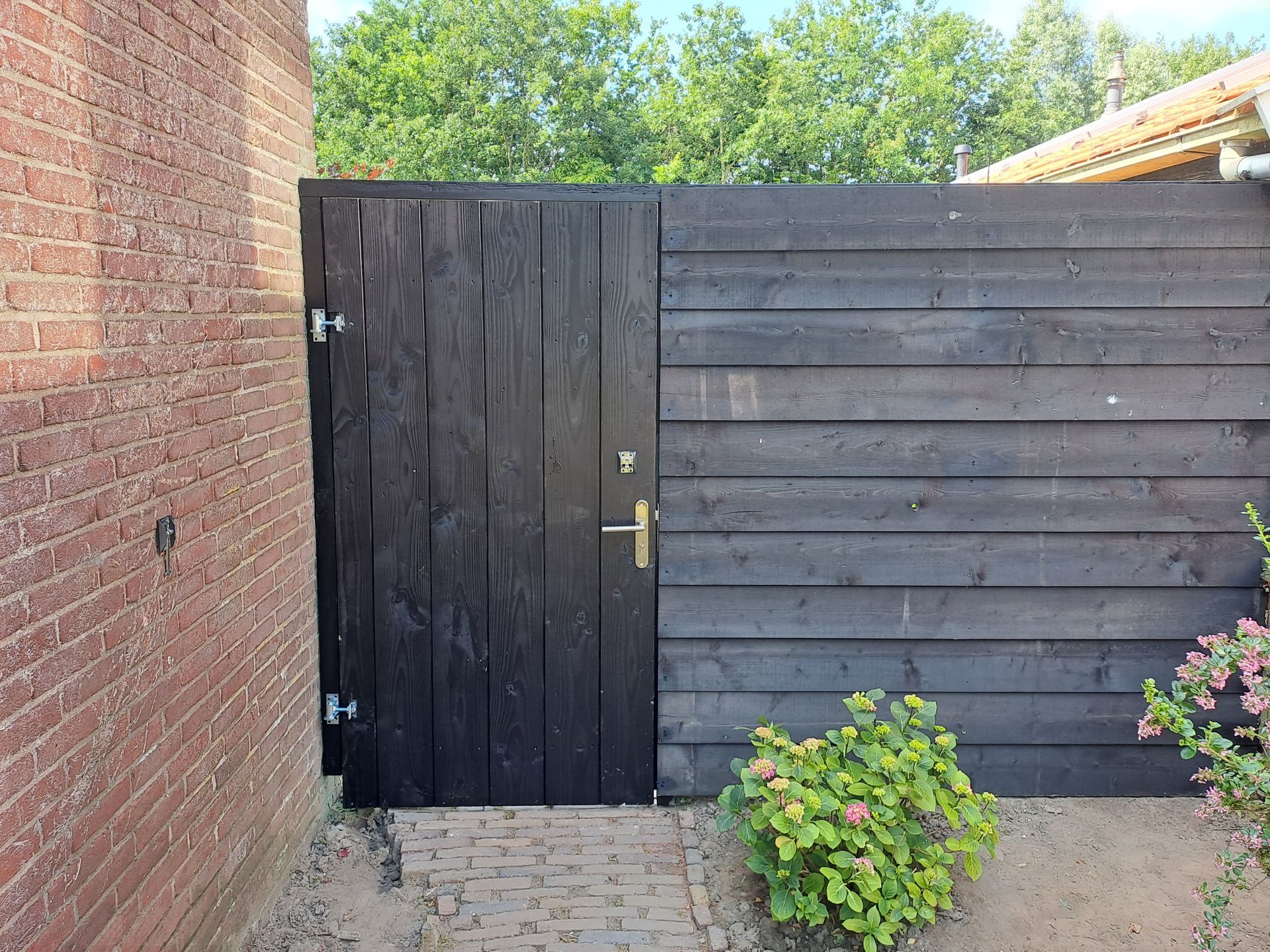 Een zwarte houten poort staat naast een bakstenen muur