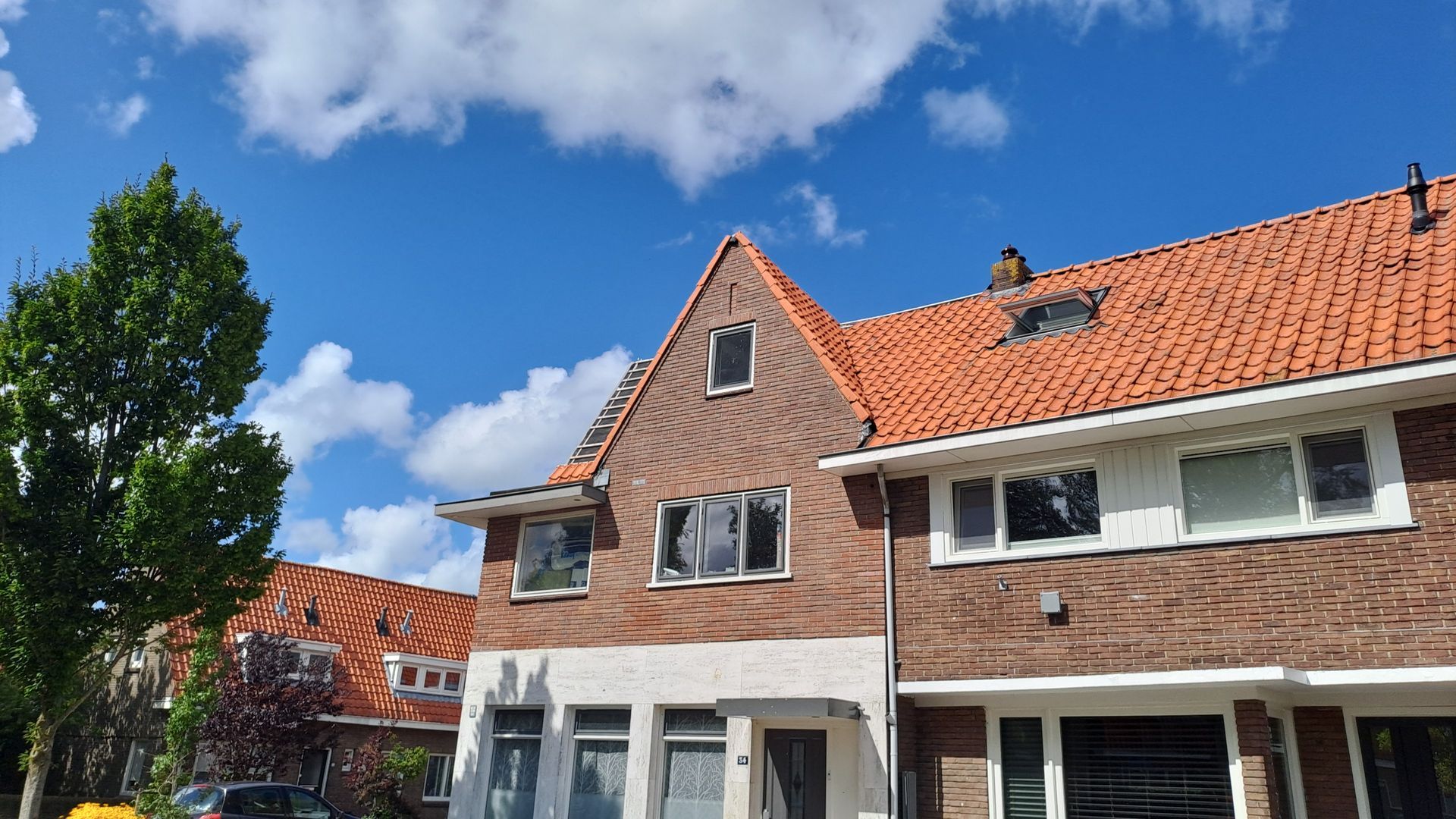 Een bakstenen huis met een rood pannendak en een auto ervoor geparkeerd.