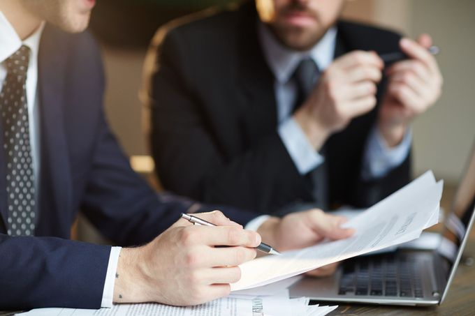 Two business professionals in suits reviewing documents, discussing strategy.