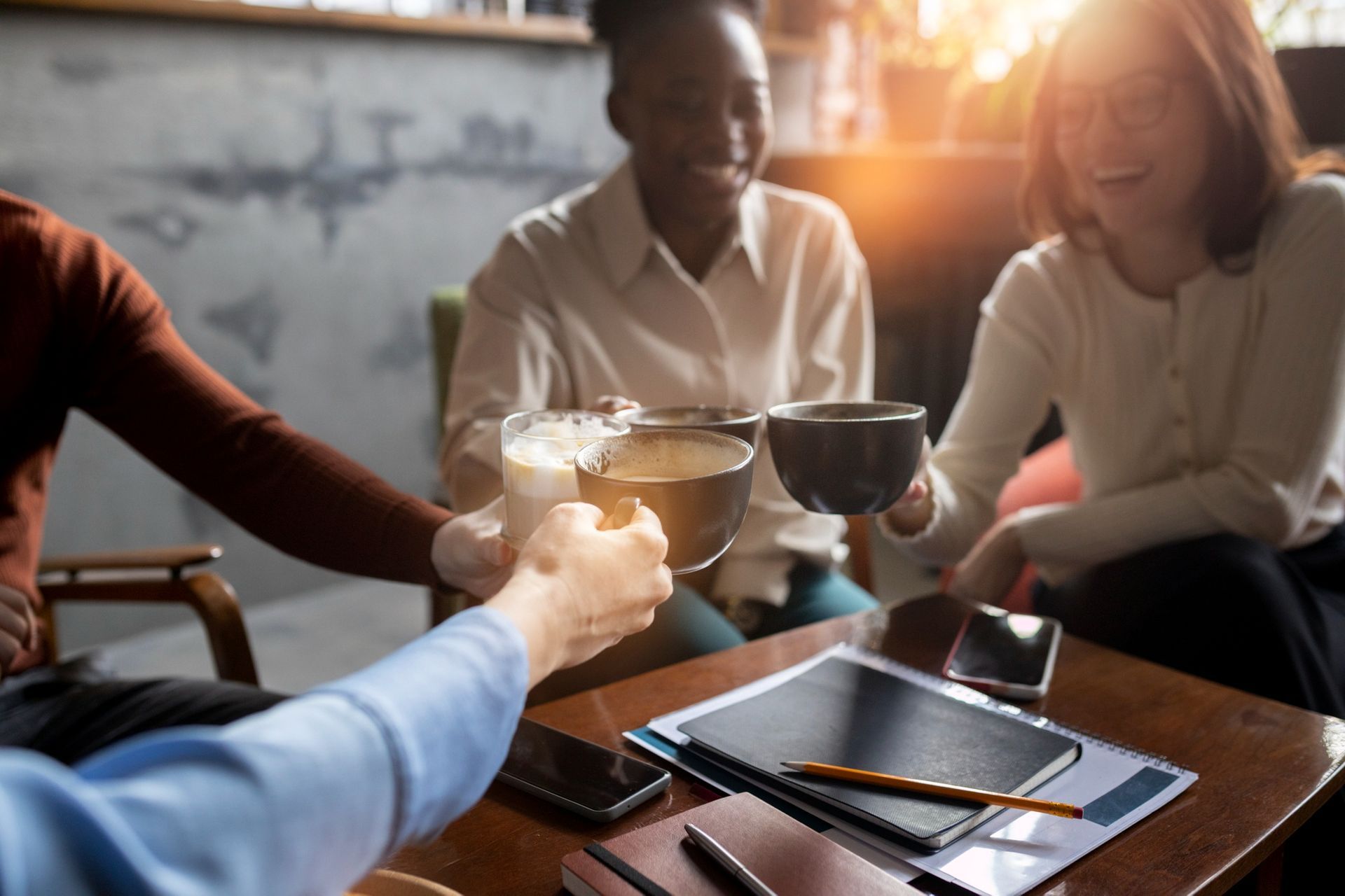 People toasting drinks in a cafe, smiling. Includes a tablet and cell phones on a table.