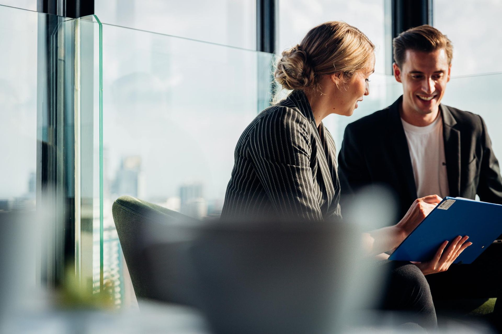 Woman and man in business attire reviewing documents, smiling in a modern office setting.