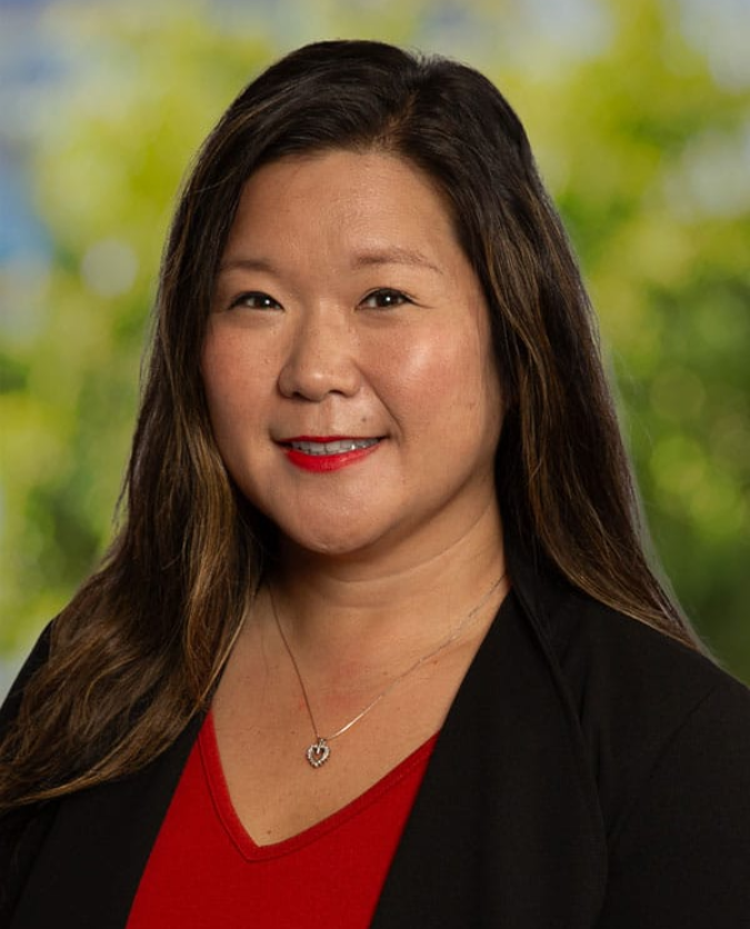 Woman with long brown hair, smiling, wearing red top and black blazer.