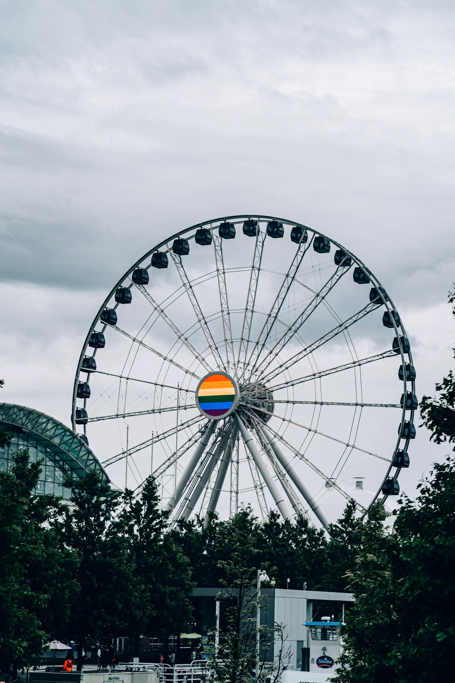 Ferris wheel with a rainbow in the center, against an overcast sky.