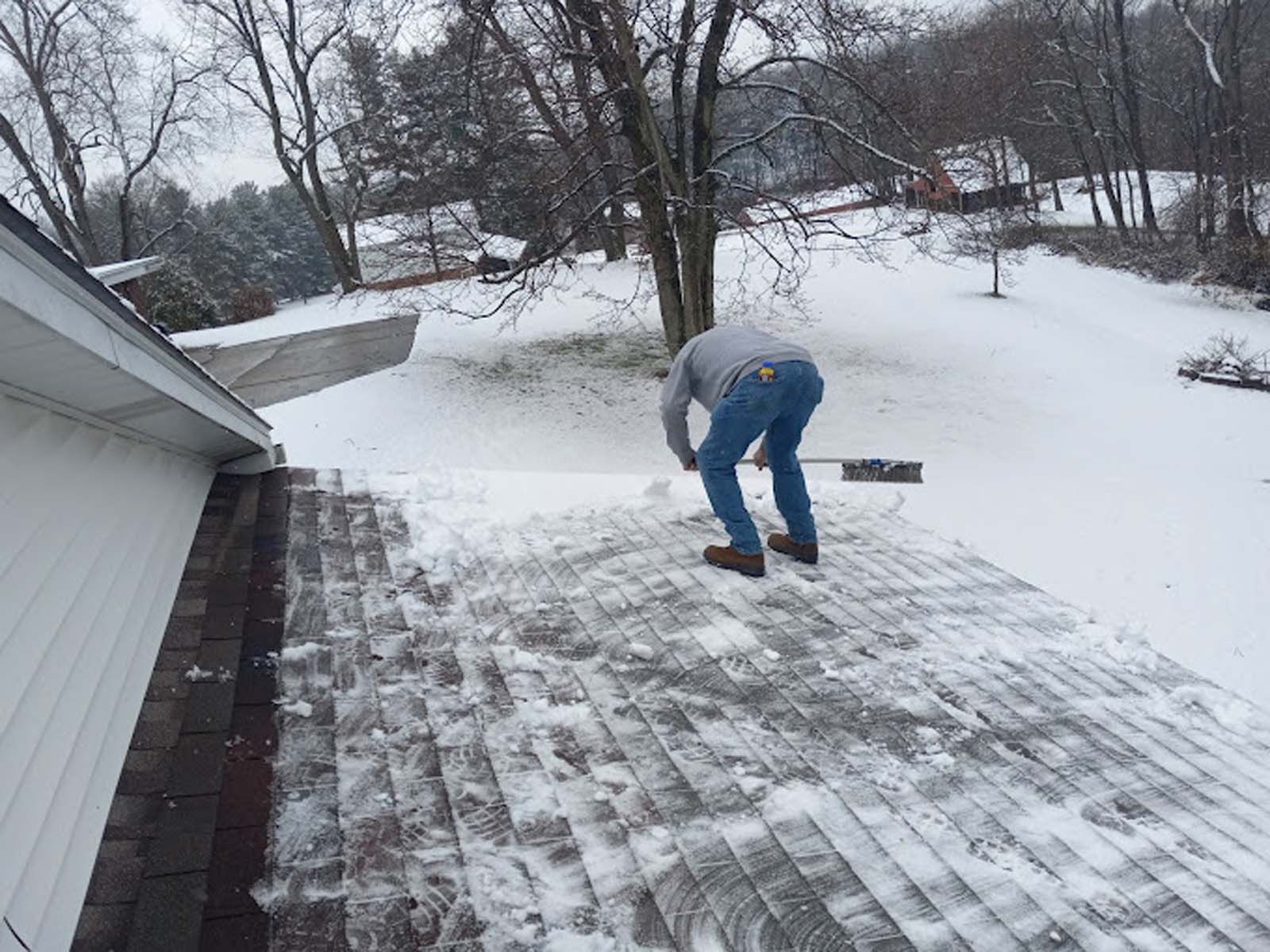 A man is shoveling snow from the roof of a house.
