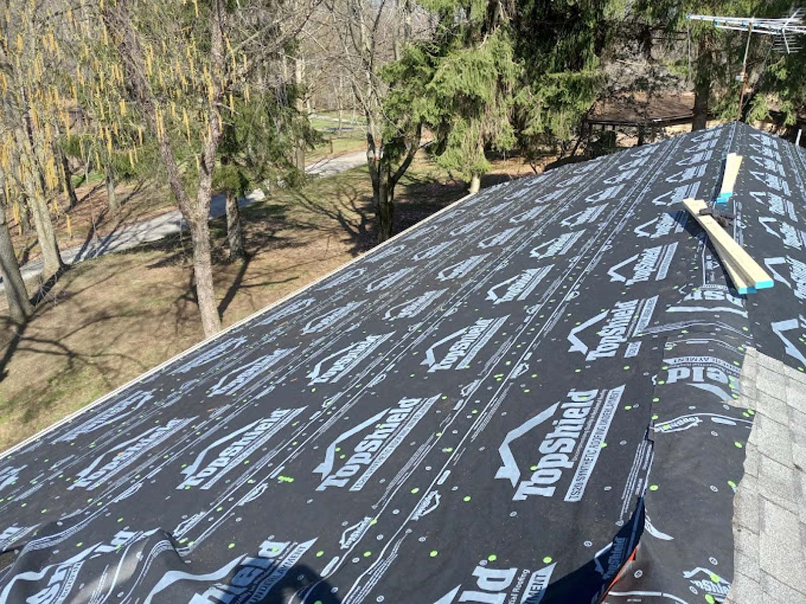 A roof is being covered with a black roofing material.