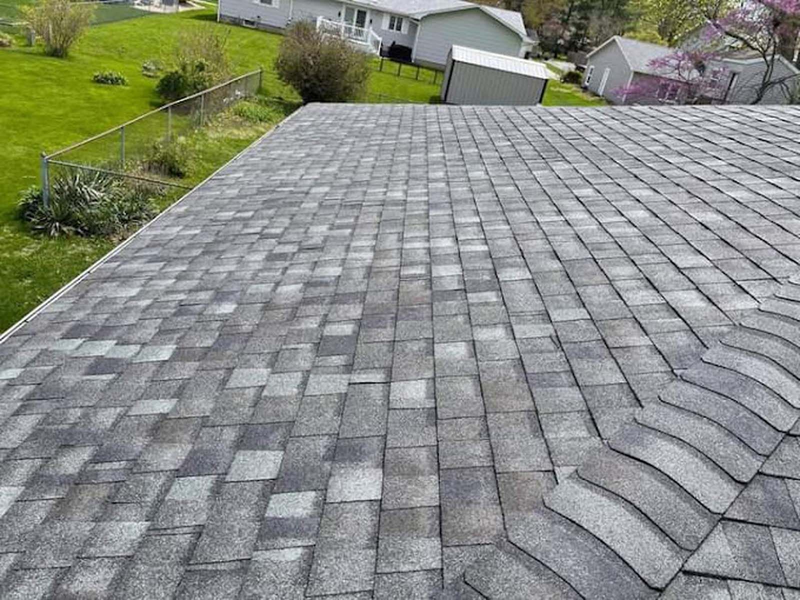 A roof with a lot of shingles on it and a house in the background.