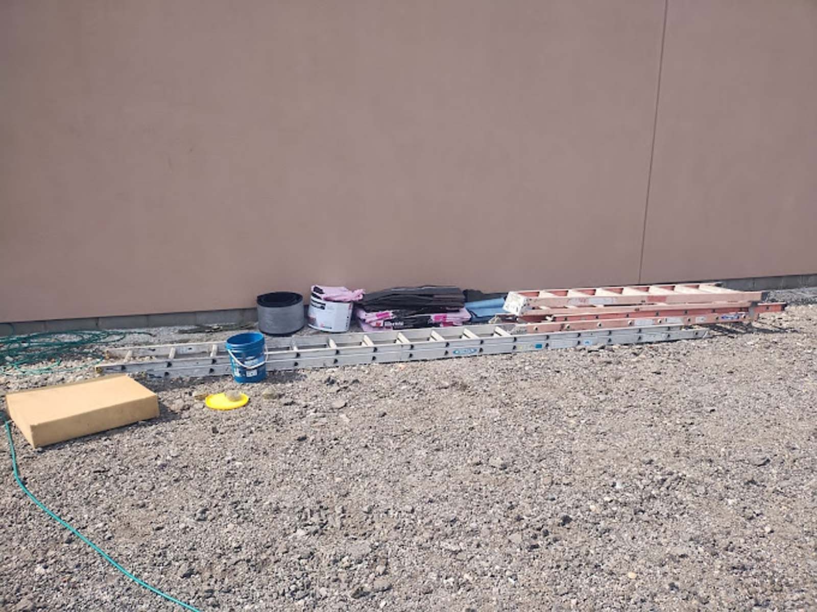 A ladder and buckets of paint are sitting on the ground in front of a building.