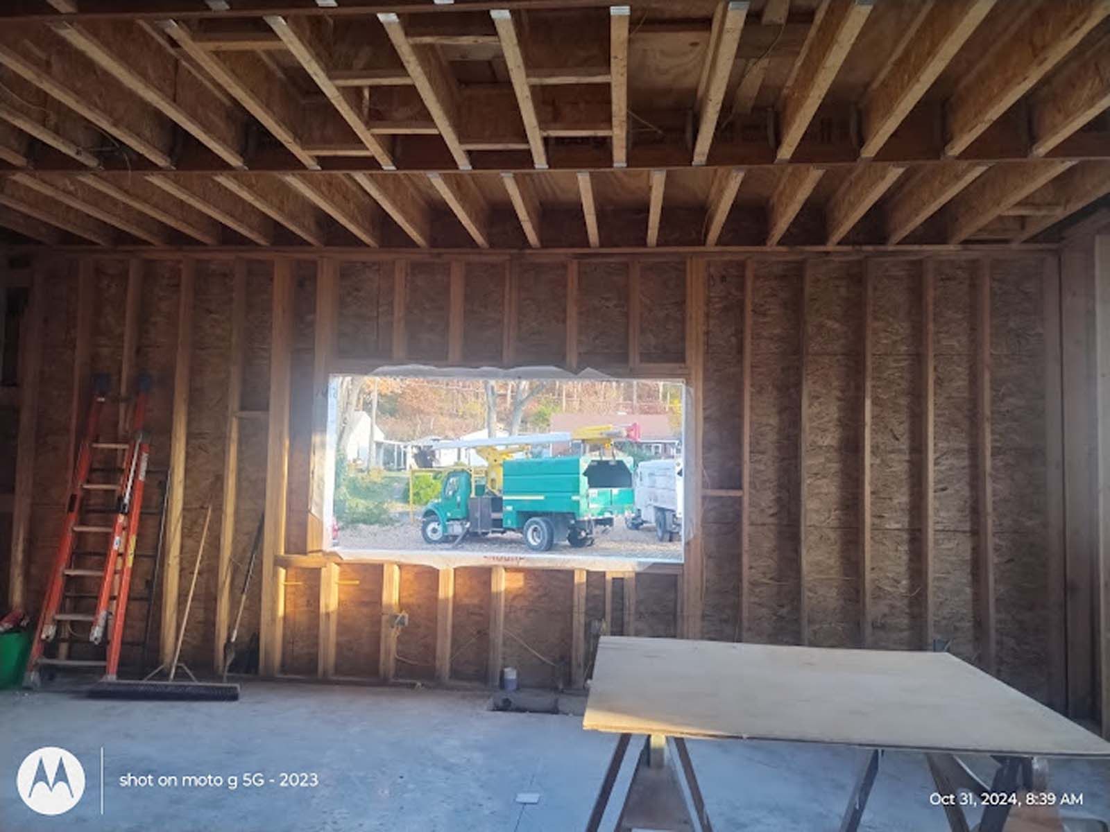 A green truck is parked in front of a window in a building under construction.