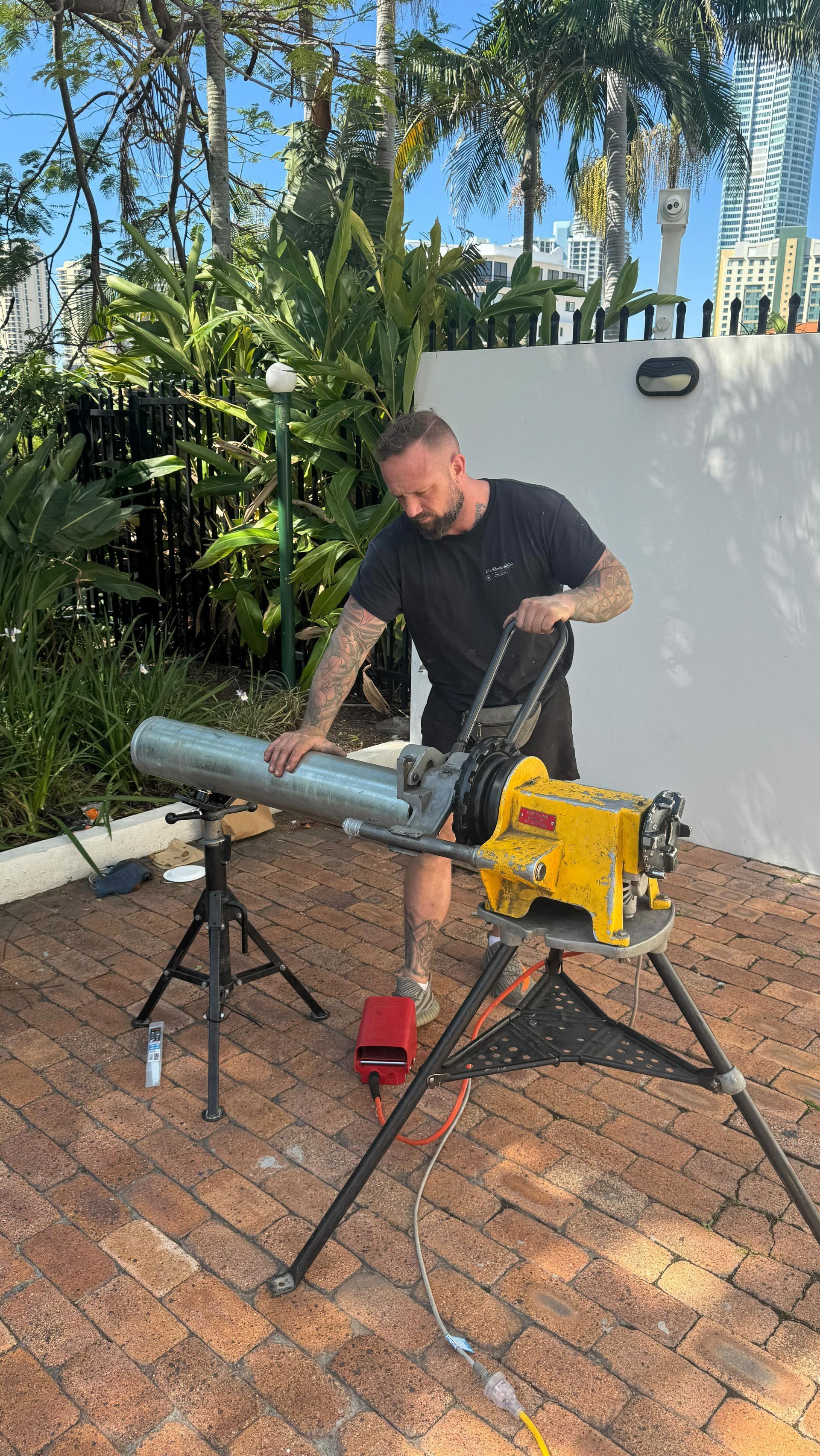 Man Cutting Metal Pipe With a Saw Outdoors — C’s Plumbing & Gas Gold Coast in Yatala, QLD