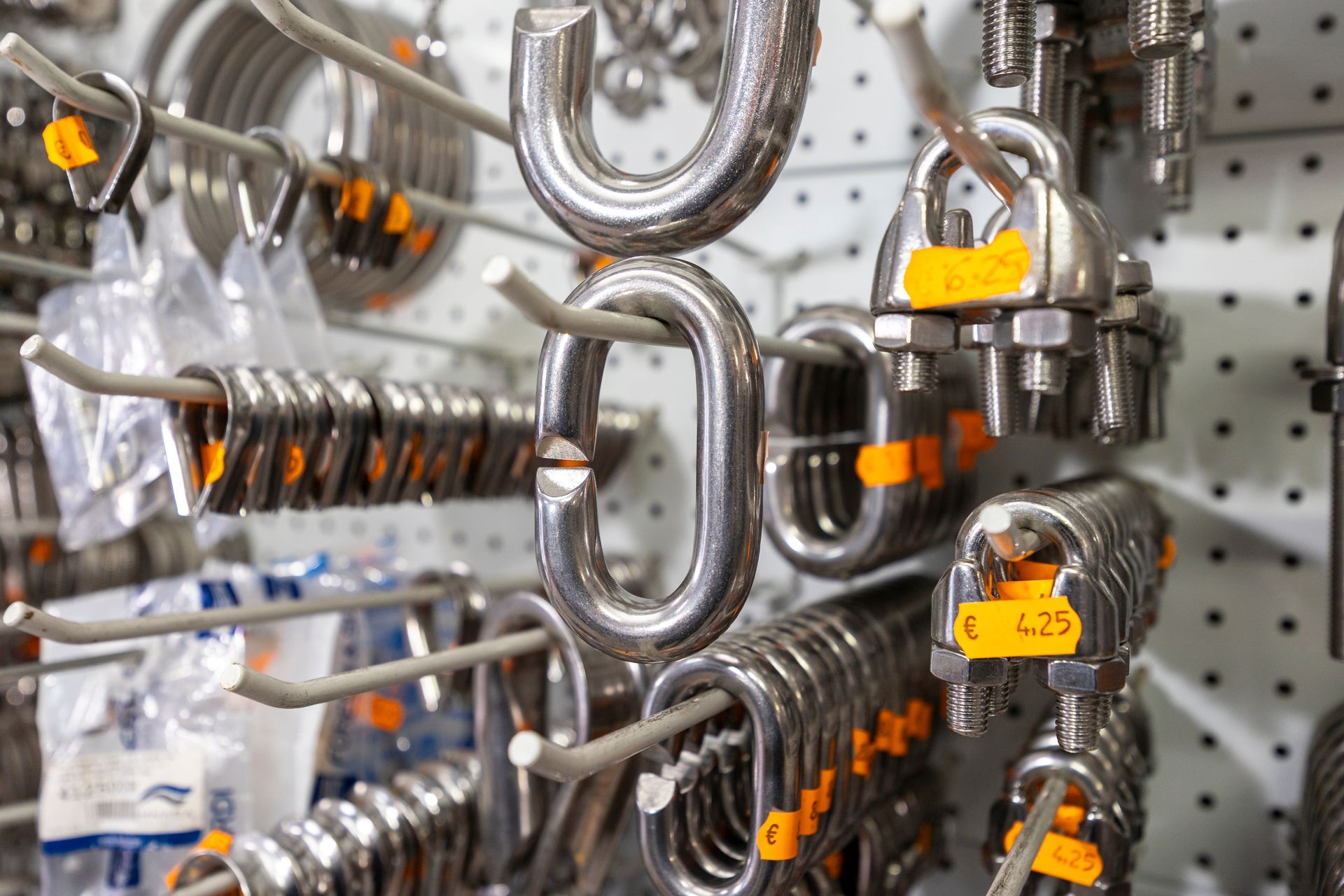 Metal hardware display; carabiners, shackles, and clips hanging on a store rack with price tags.