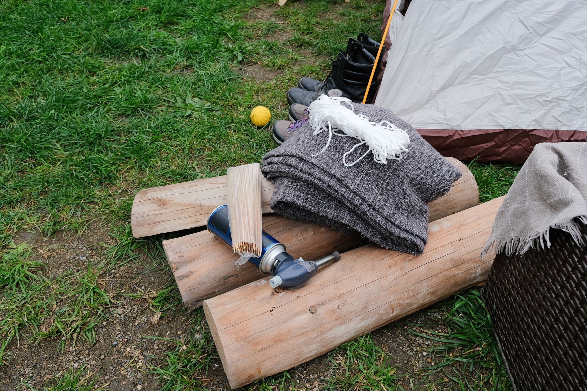 Logs, drill, and blanket on grass, near a tent.