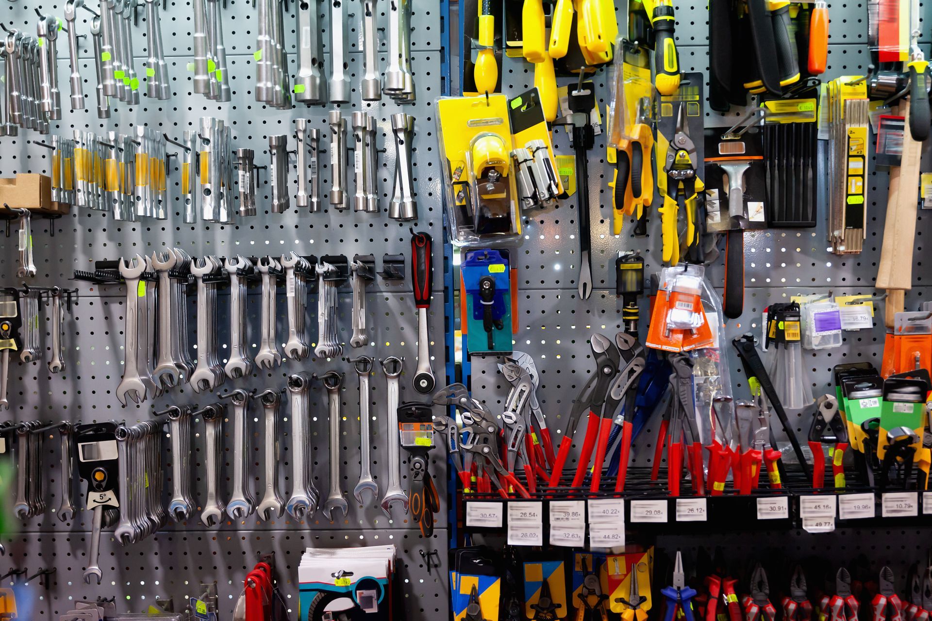 Tools displayed on a pegboard in a hardware store, including wrenches, screwdrivers, and pliers.