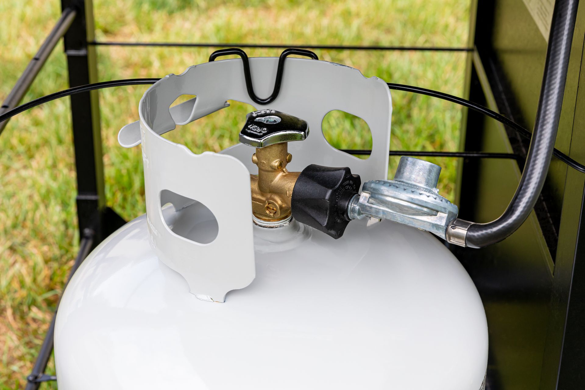 White propane tank with connected valve and hose, set against green grass.