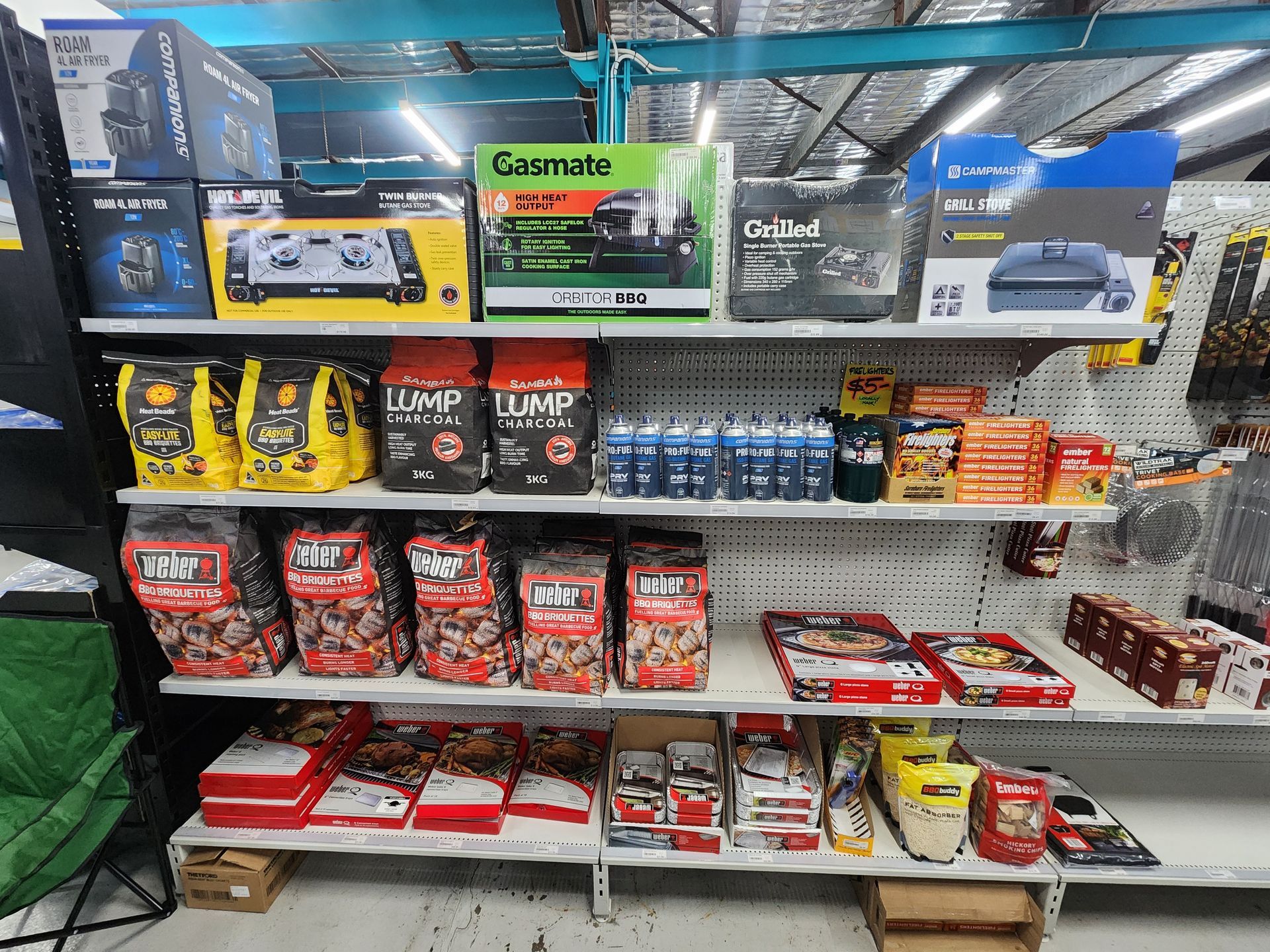 Shelves stocked with camping supplies, including cooking gear, food, and fuel, in a retail store.