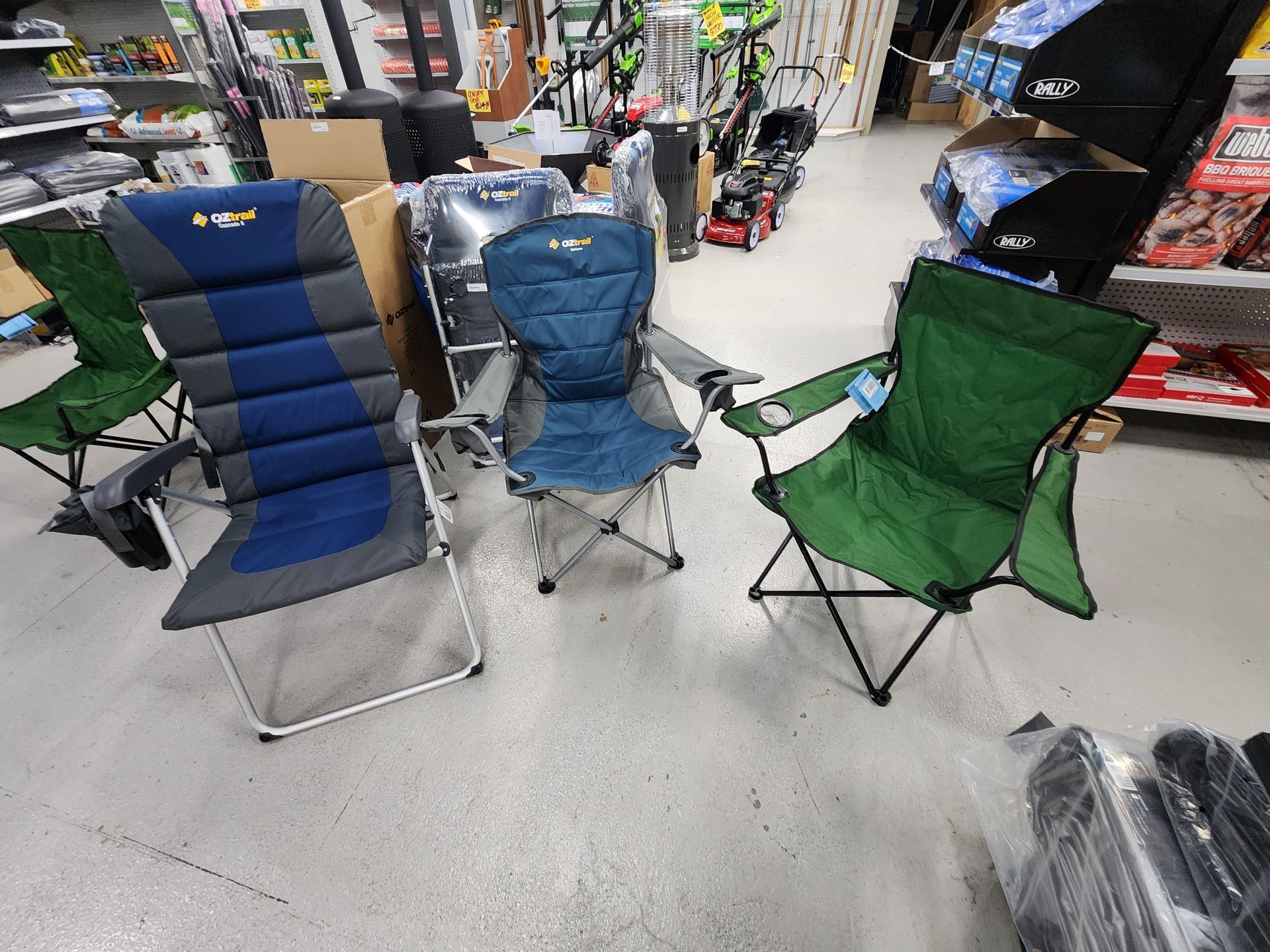 Three folding outdoor chairs on display in a store; blue, green, and gray.