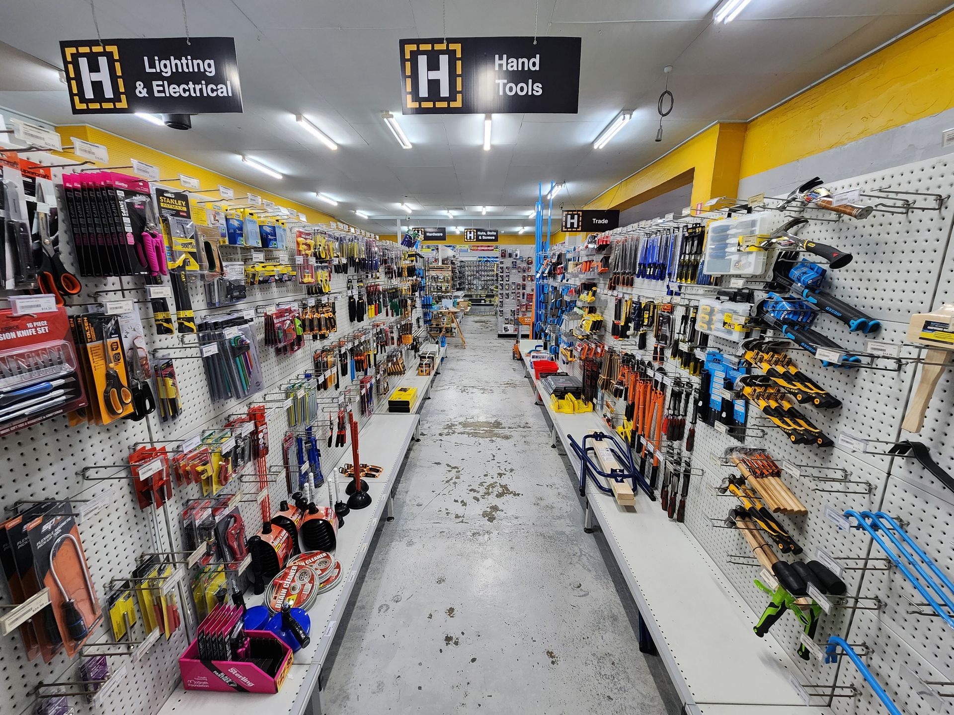 Hardware store aisle with tools displayed on white pegboards under fluorescent lights.