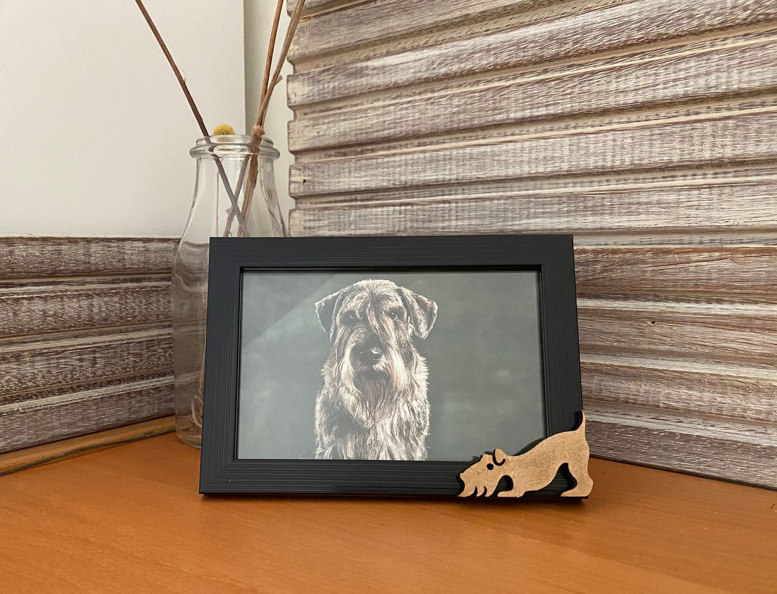 Hoekdisplay: houten plaat, ingelijste foto van een hond, glazen fles met gele bloemen.